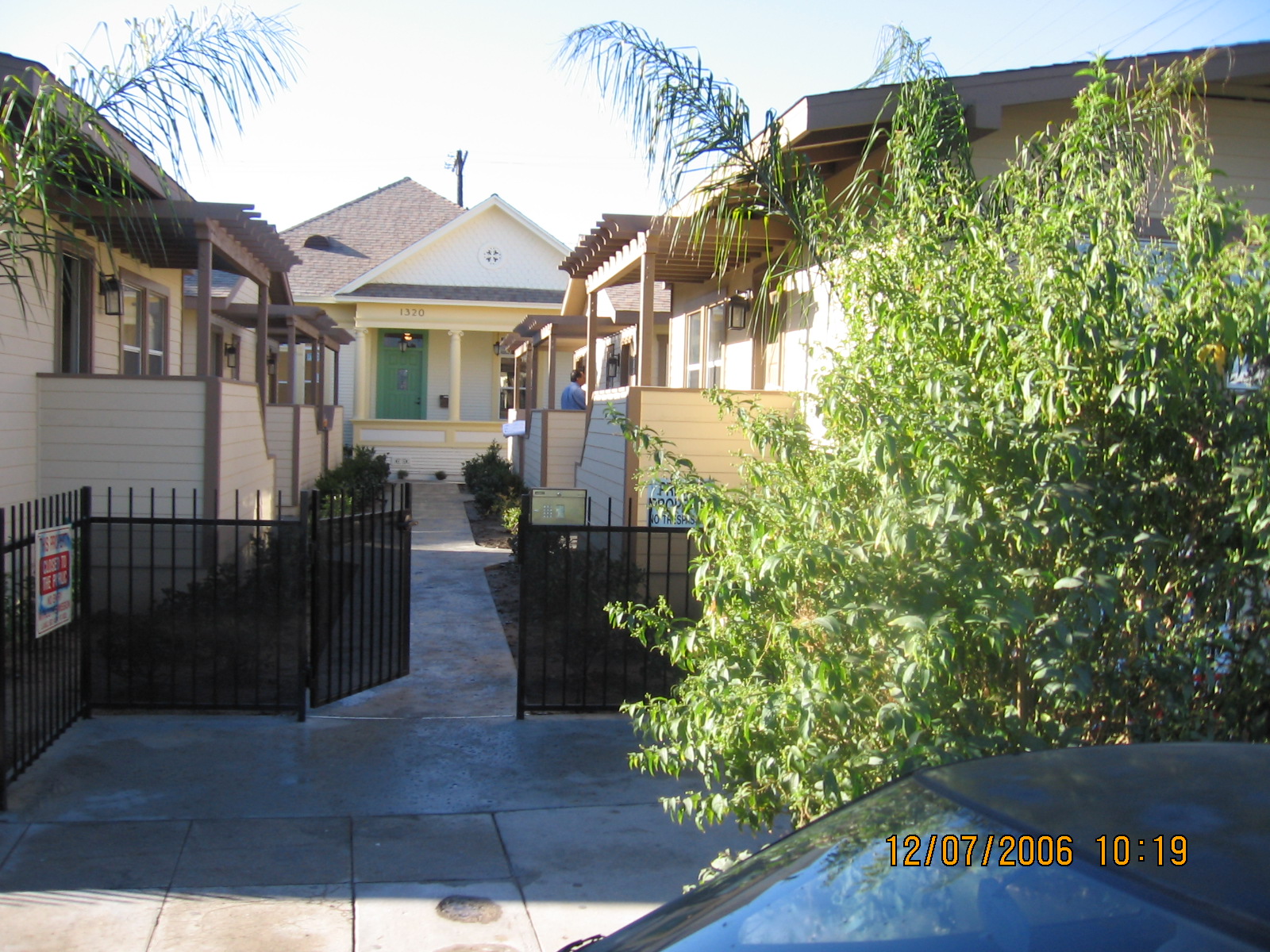 Gated group of one story complexes. Entry is ground level with 3 stairs to access the unit and has a key pad. Small bushes are aligned in the front of each complex. One complex has a triangle-patterned curtain near its front door.
