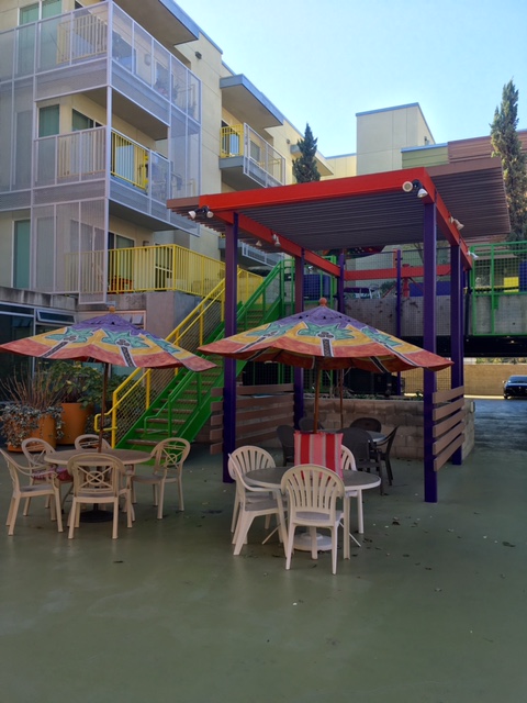 Outdoor patio that includes tables with umbrellas for shade, chairs , and a covered area.