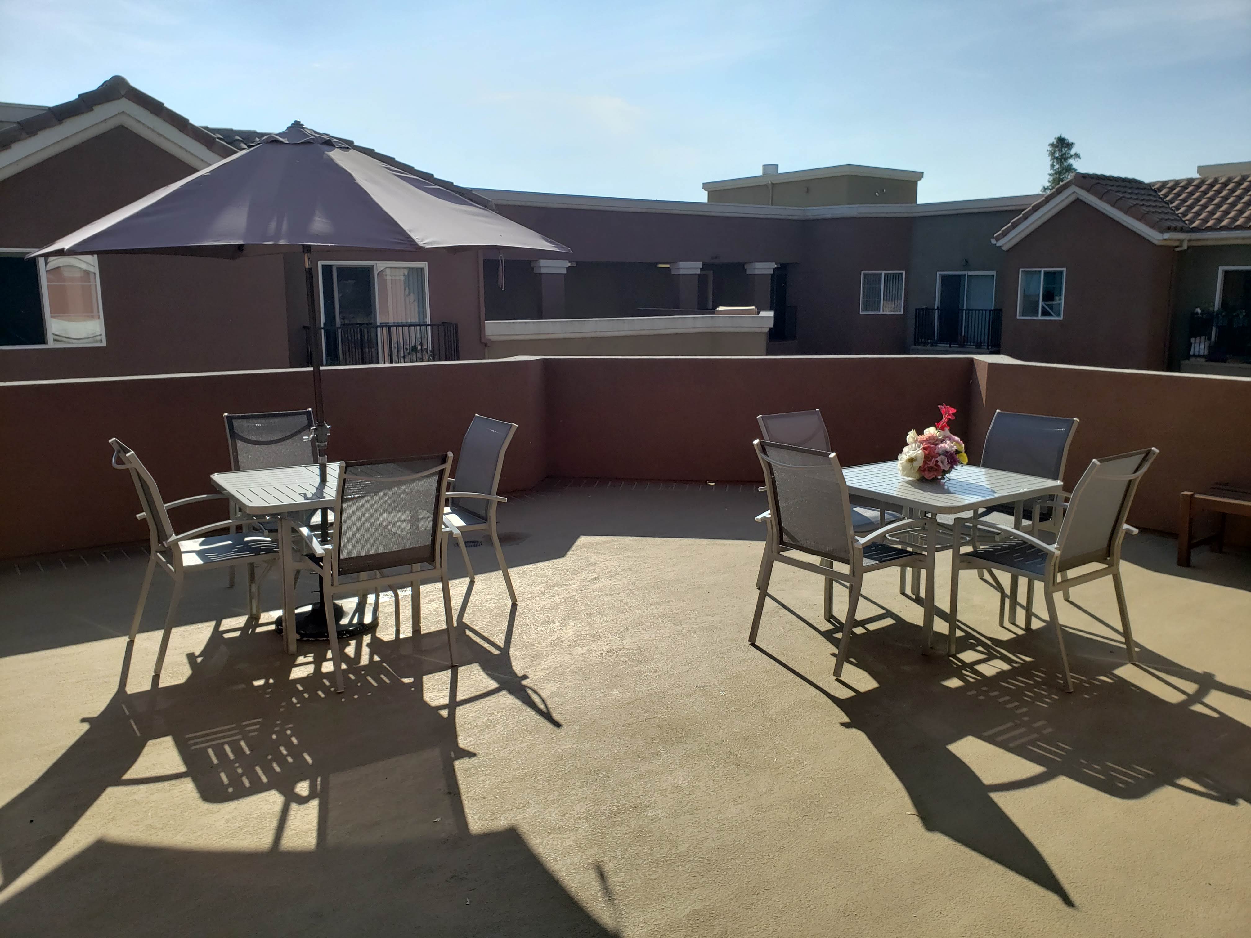 Image of vintage crossing senior apartments upper level community patio. Patio table and chairs. one patio set has an umbrella for additional shading. small decrative flower on table