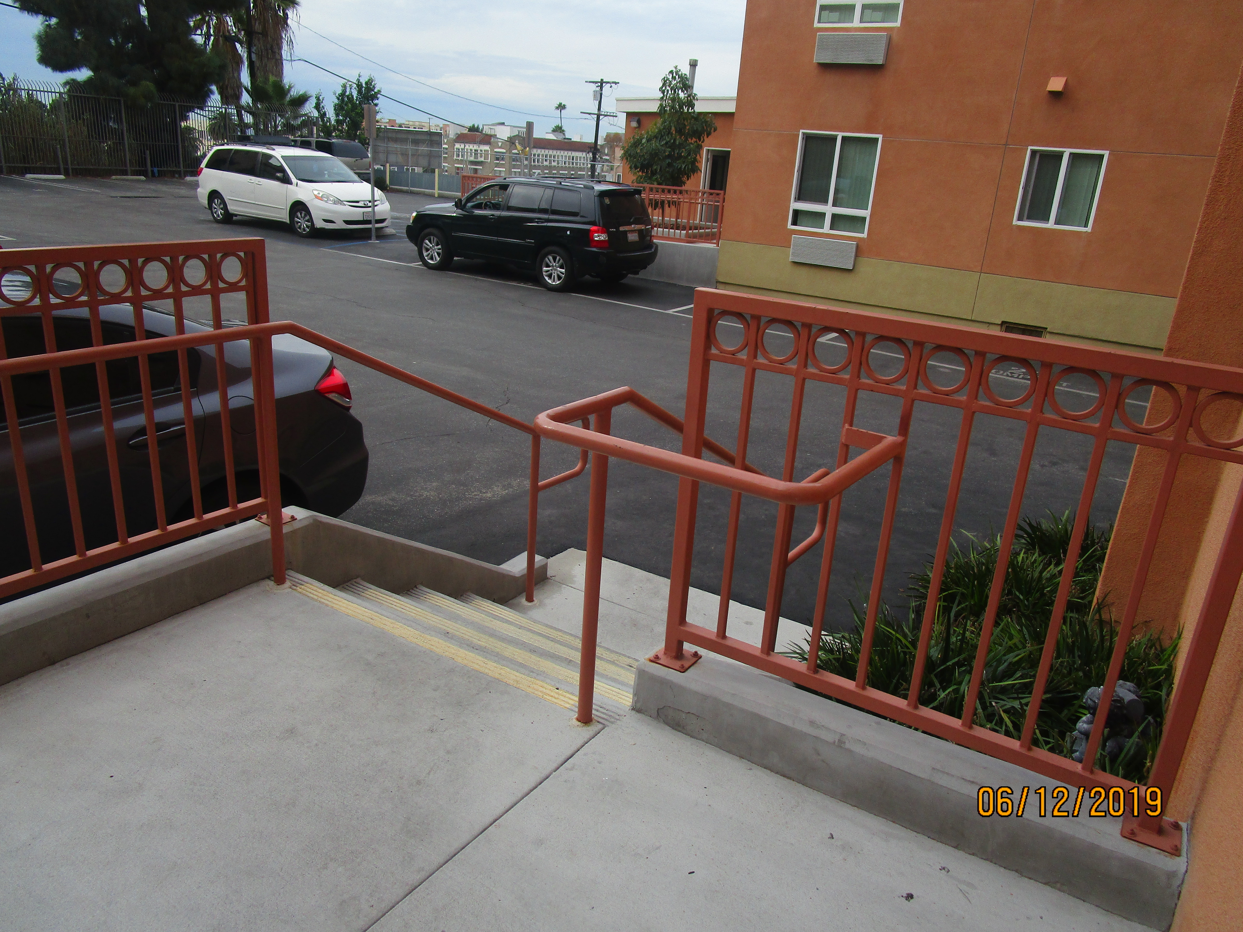 Front view of a four concrete steps with handrails on each side, parking view, parked cars,