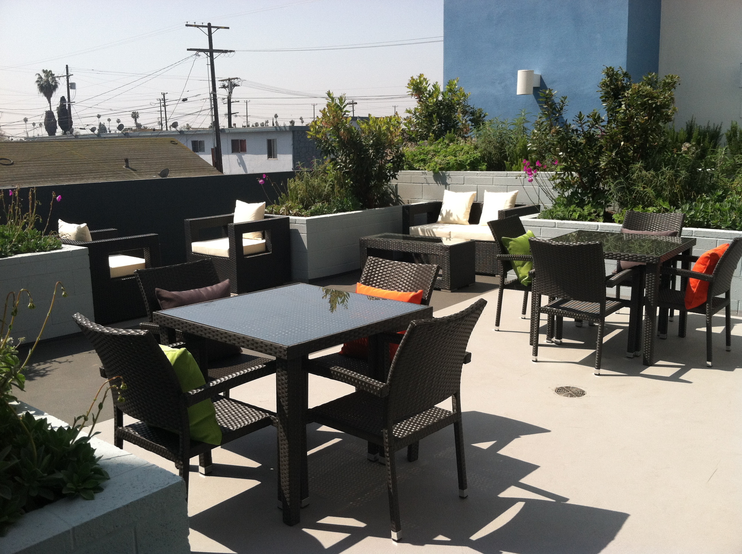 Rooftop lounging area. It has multiple chairs and tables. There is also various plants surrounding the seating areas.