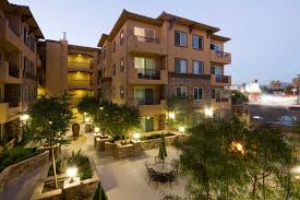 Exterior view of Adalucia Senior Apartments. 4 story building with large courtyard, embrella table and green lanscaping