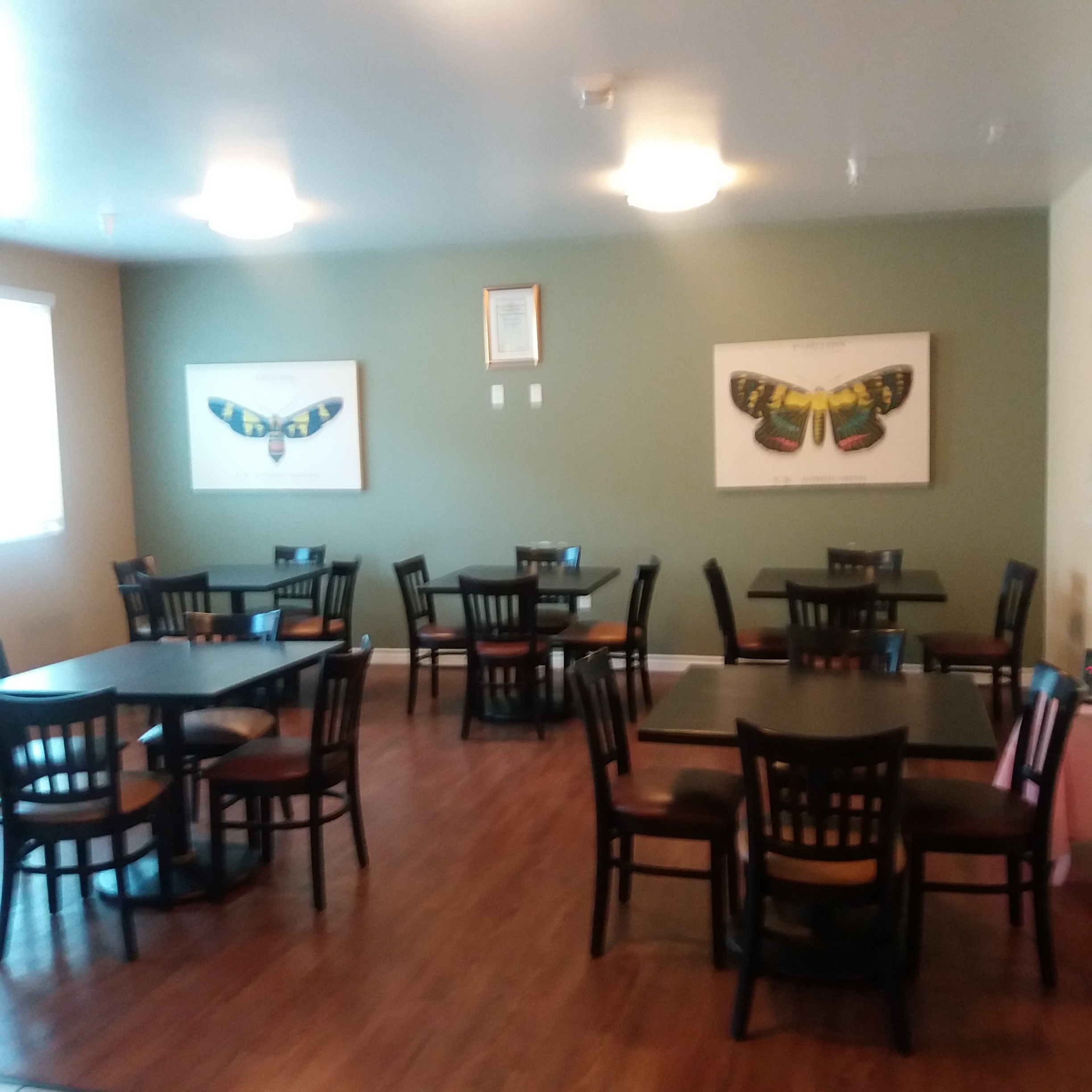 Community room with multiple four seat dining tables. There are two butterfly art pieces on the wall, and the flooring is wood.