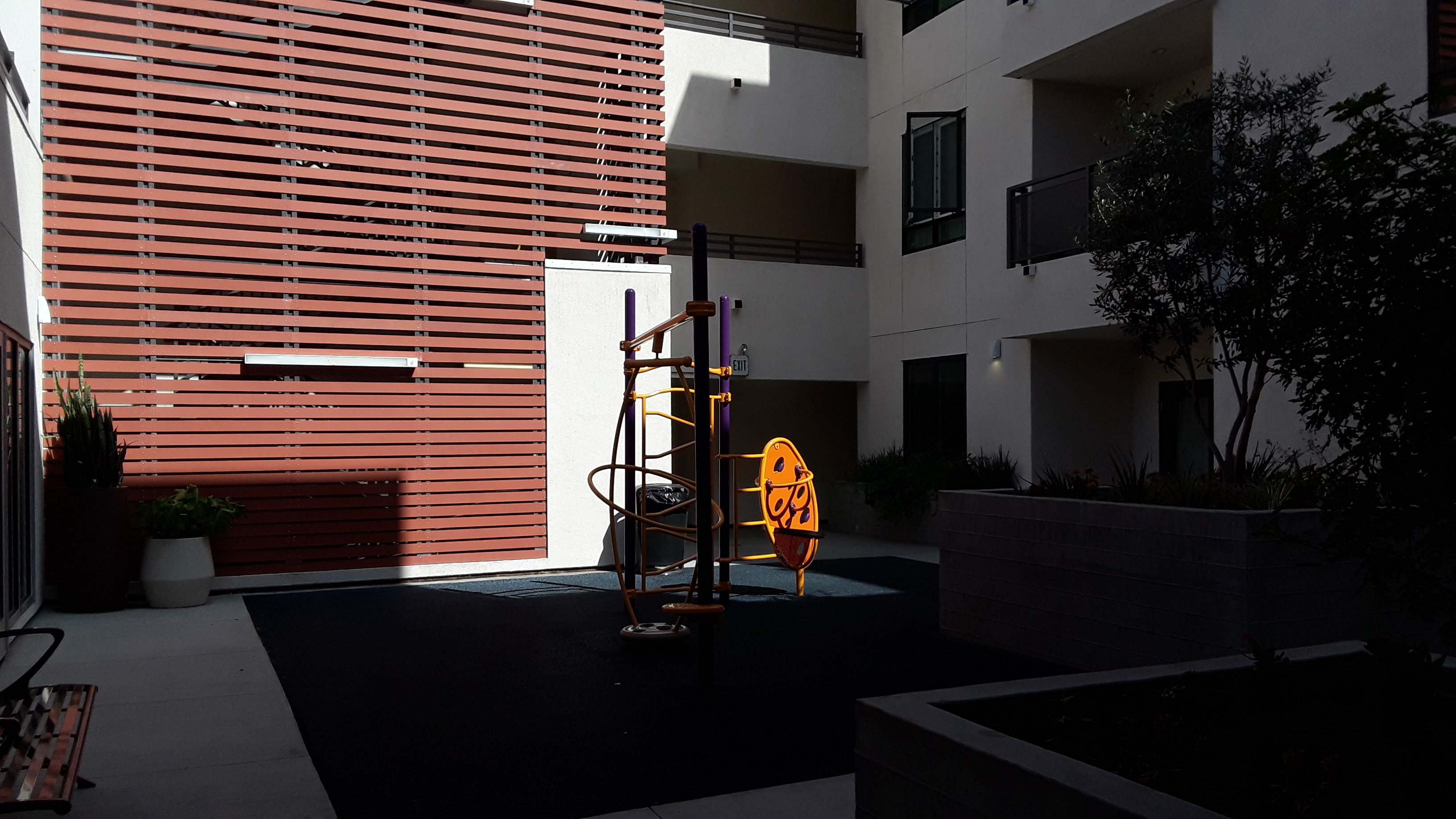 Nice playground, yellow, orange and purple climbing equipment, plants and balconies around it.