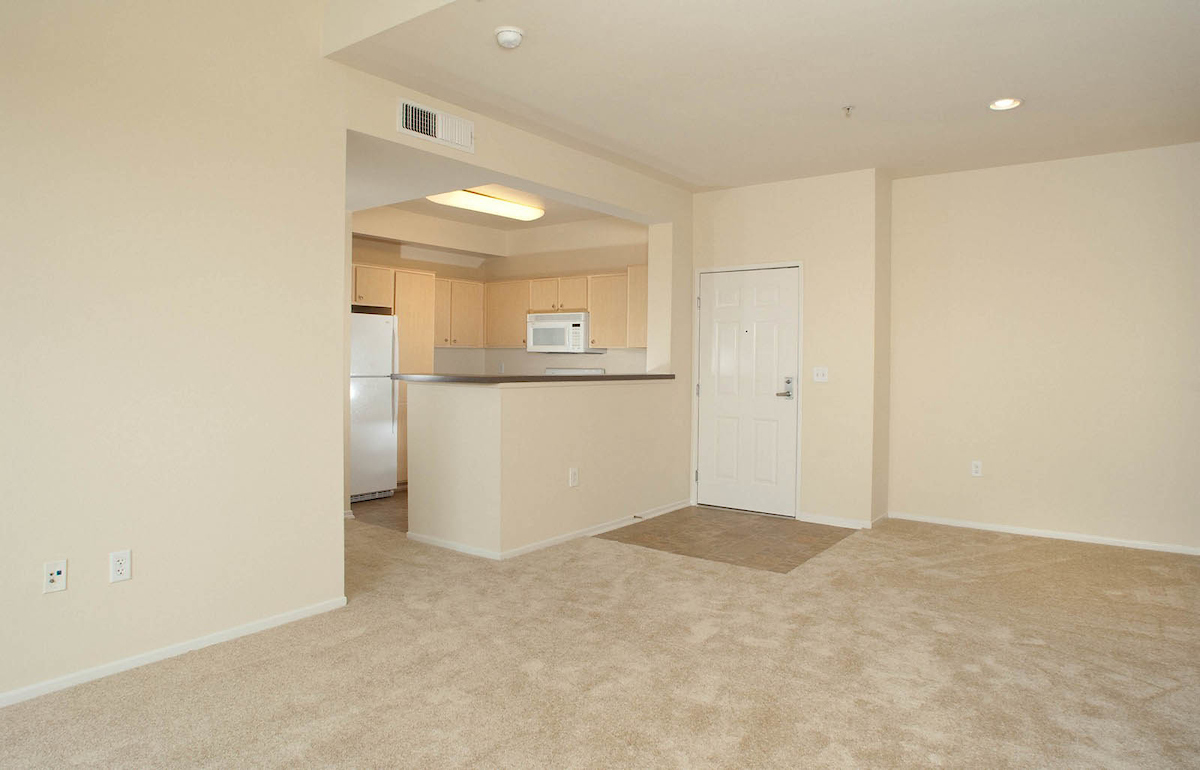 sample of Fountain Park unit living room area. white carpets, access to kitchen near front door.