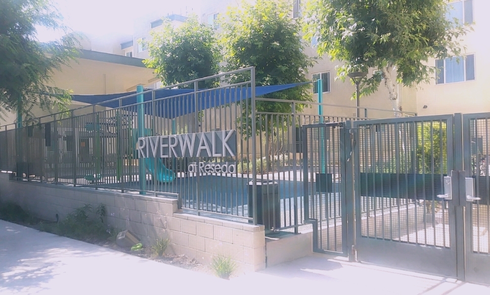 Street view of Riverwalk at Reseda Apartments. Gated building with a playground and landscaping.