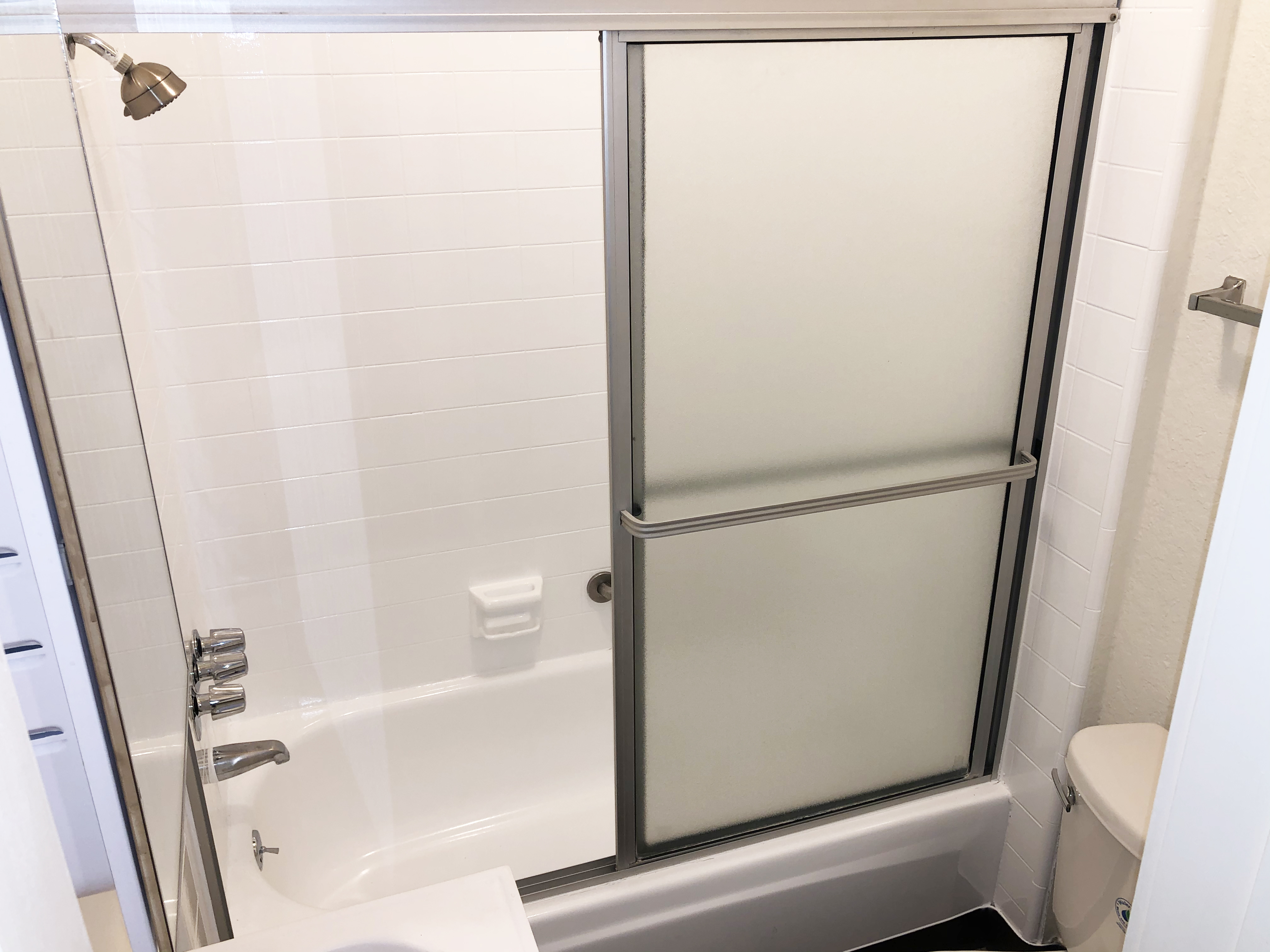 Close up view of the restroom showing the bathtub with showing and sliding door.