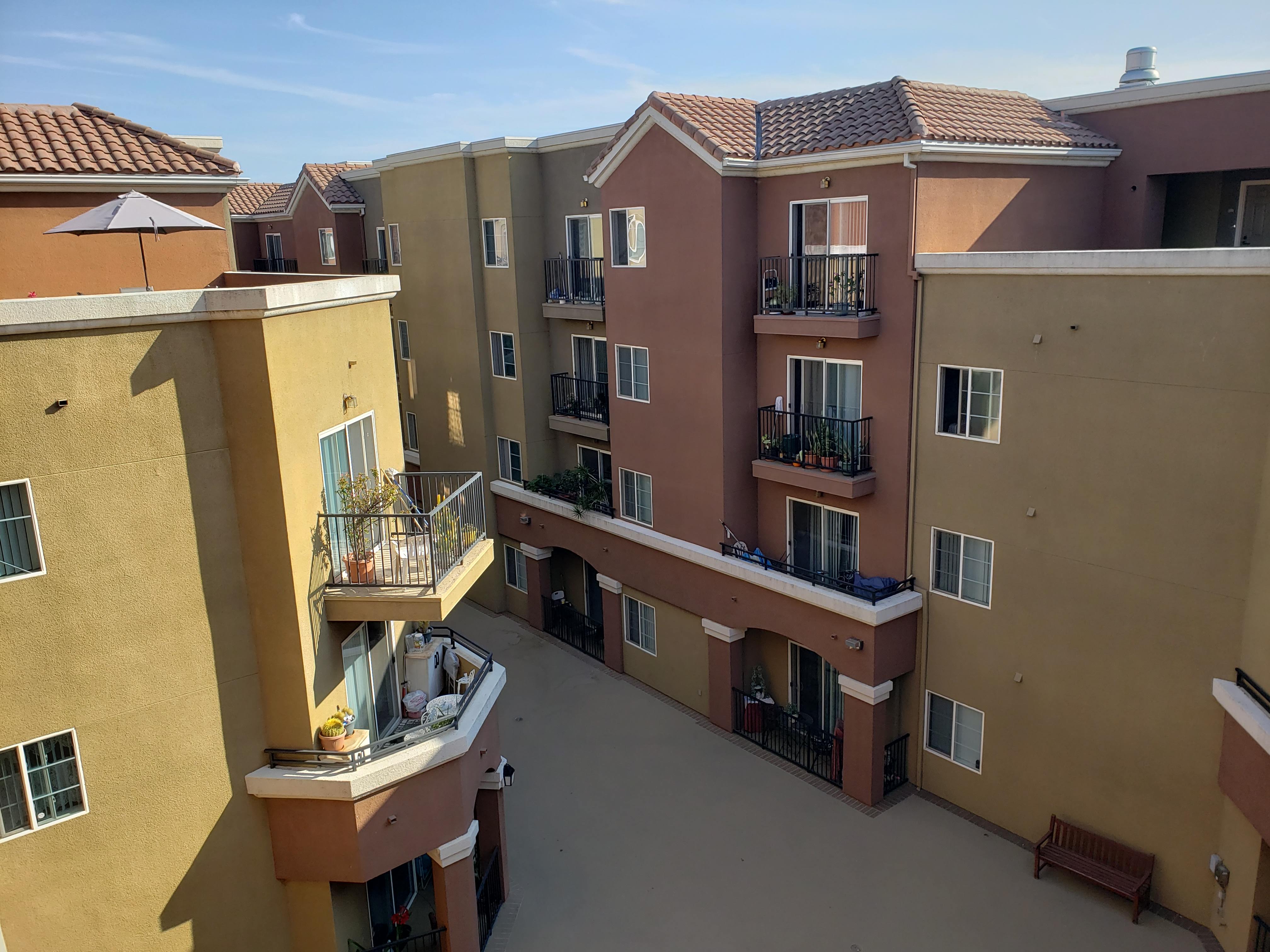 Image of vintage crossing senior apartments courtyard. Image taken from top floor. large courtyard with bench seating. Units with balcony access. some balconys with plants and misellaneous objects.