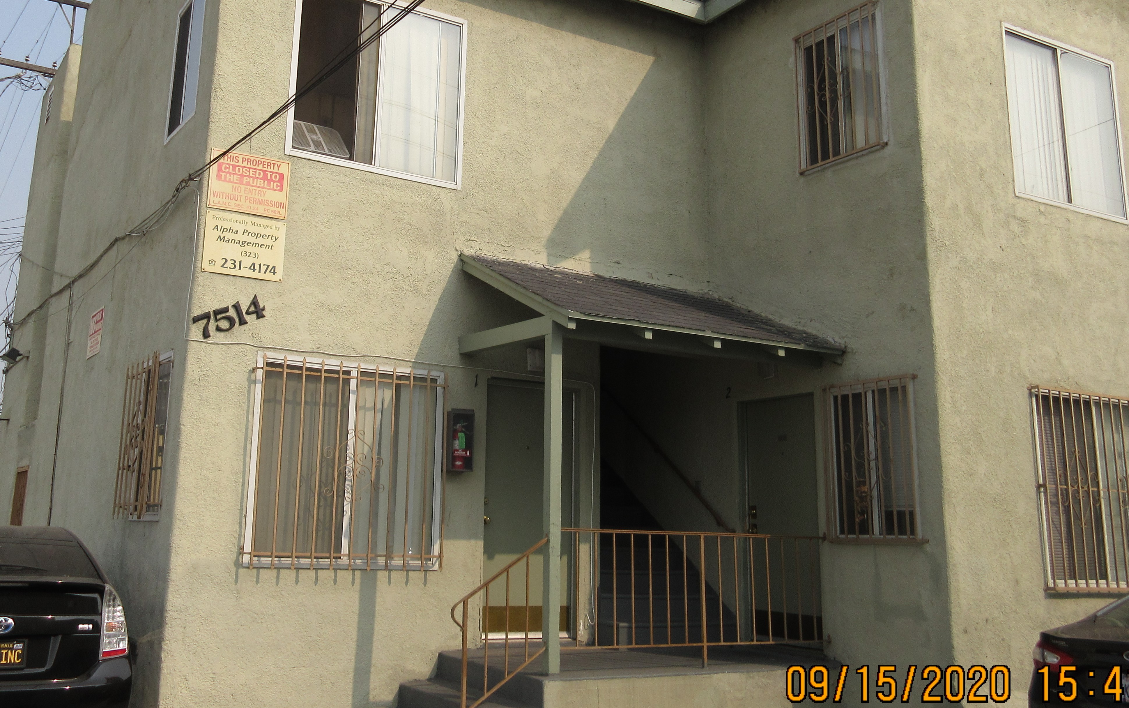 View of a two story building, steps with handrails, bottom windows with security gates, building number and private property on the left side.