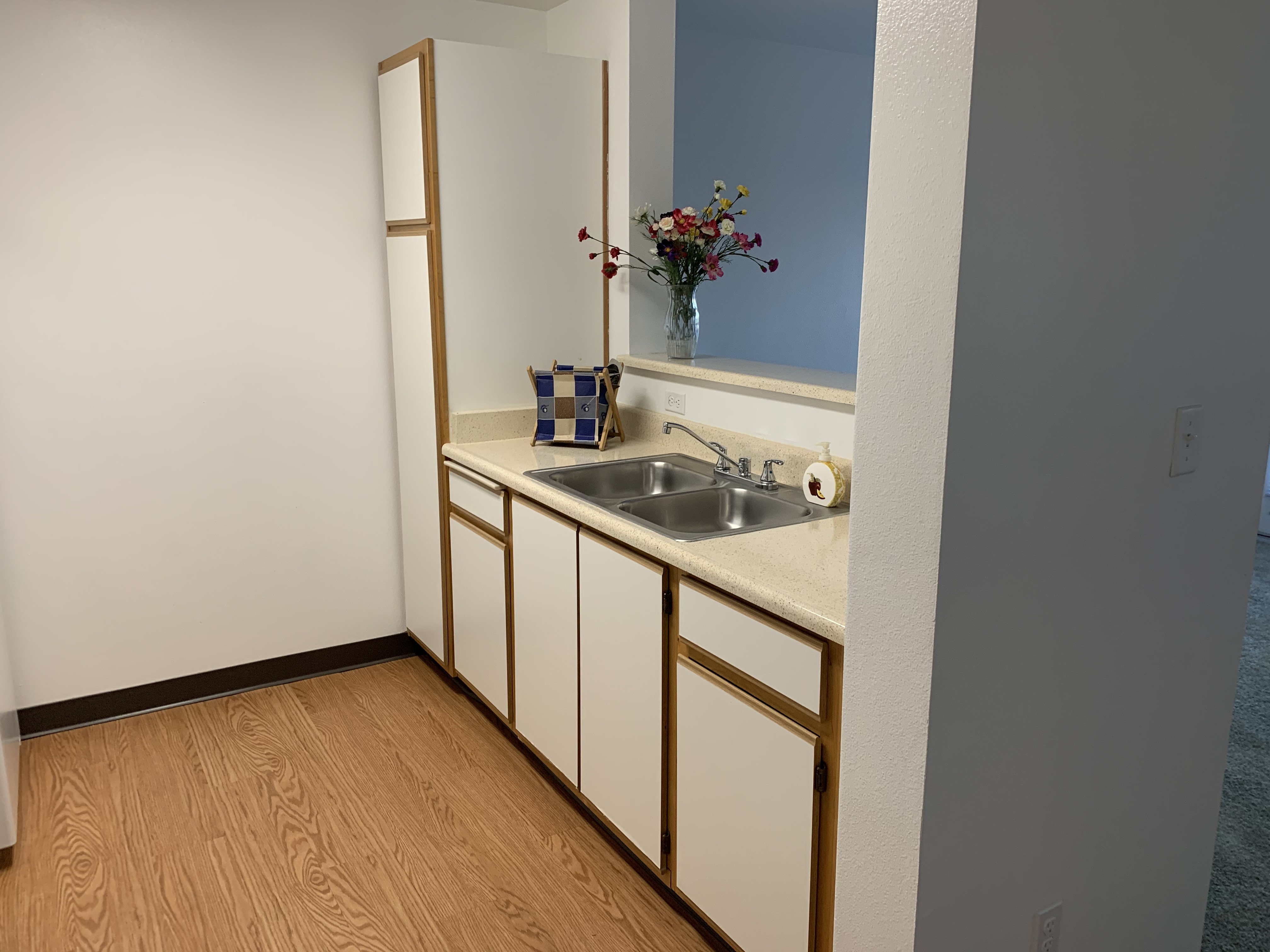 Different angle of a kitchen area. Pictured is the sink, more cabinets and an open window counter.