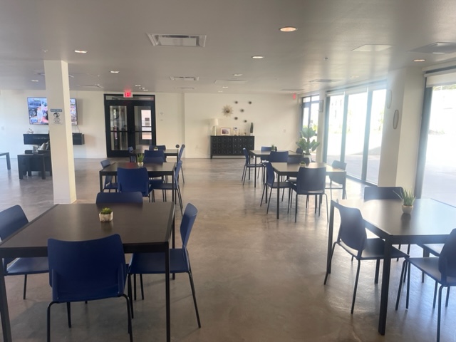 RDC- Community Dining Room with tables and four chairs per table. Large windows on the right.