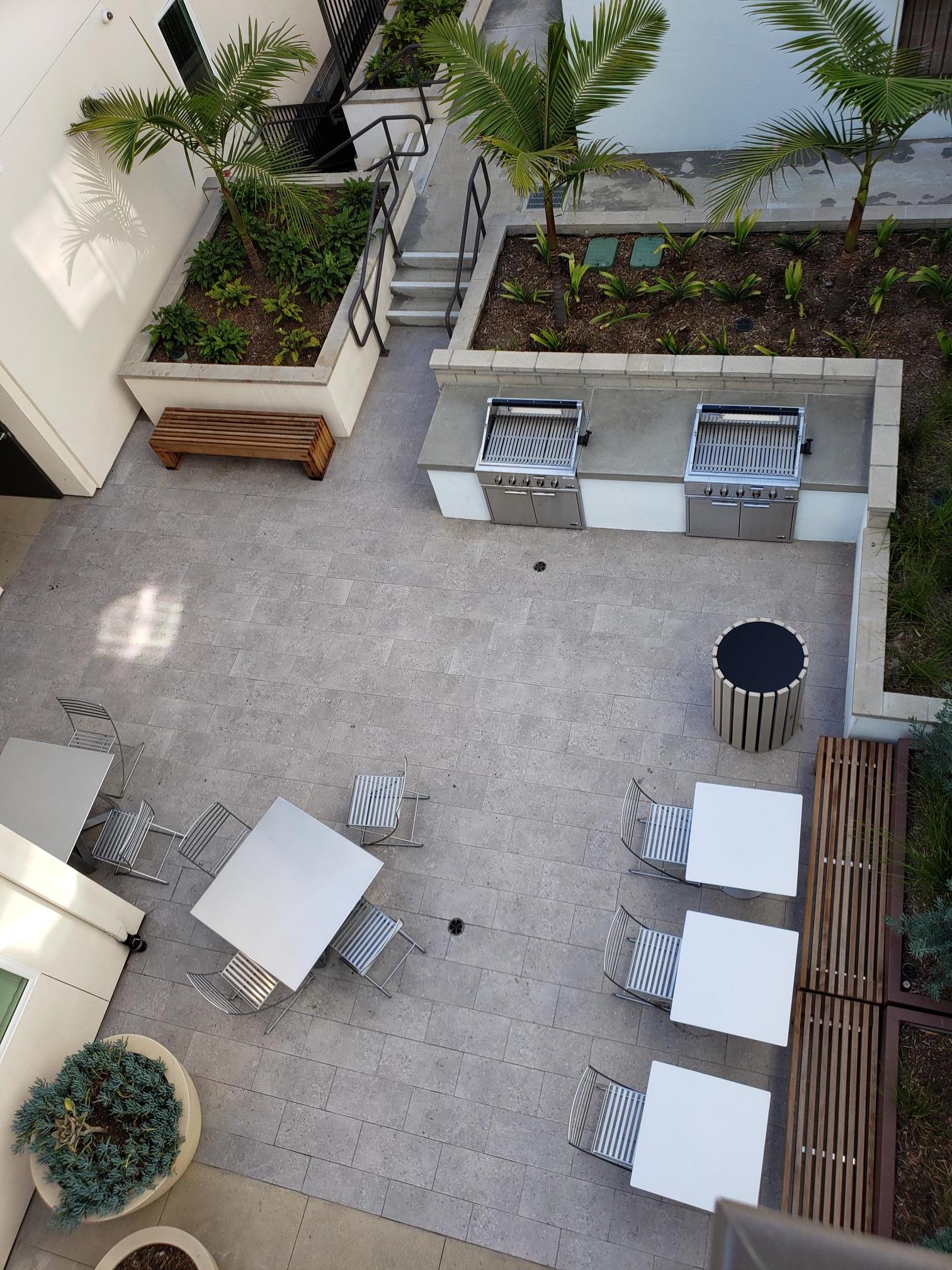 view of Coreonel Apartments courtyard from upper level . Within courtyard there are several patio table and chairs. Large planters located in area. BBQ grill available