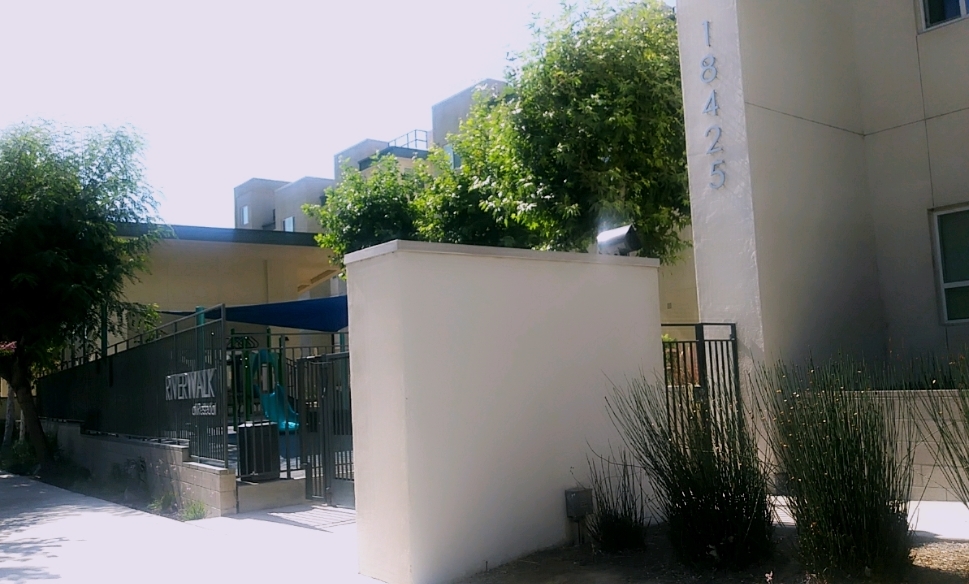 Street view of Riverwalk at Resada Apartments. White building with blue accents and landscaping