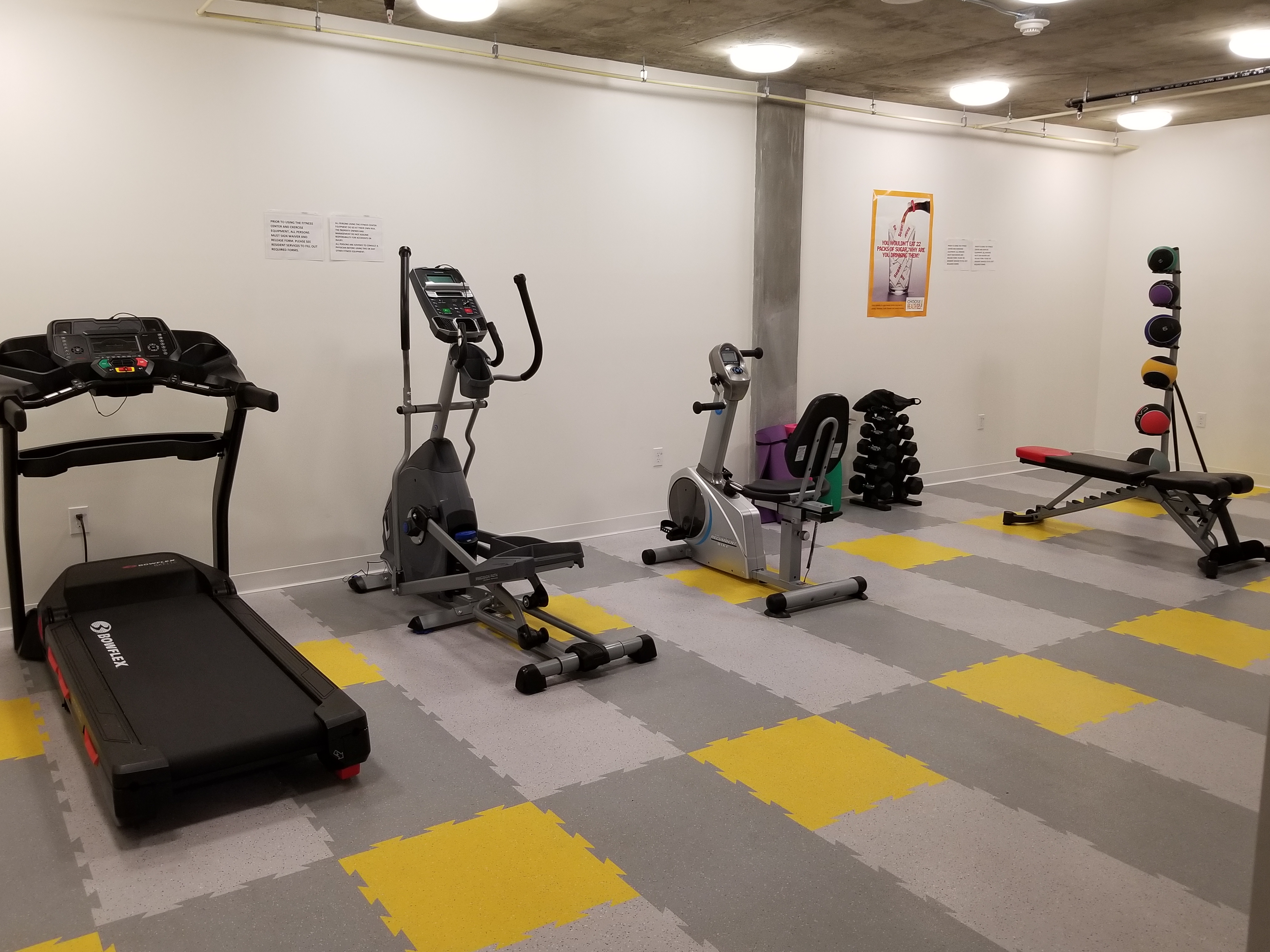 Fitness room that consists of a treadmill, stationary bikes, elliptical machine, a flat becnh and weights.