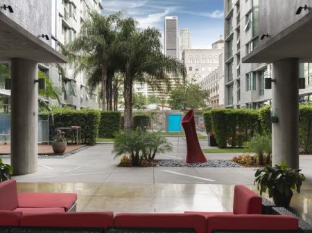 Courtyard with plants, hedges, trees and small grass areas. This view has a lounging area with a large red sofa.