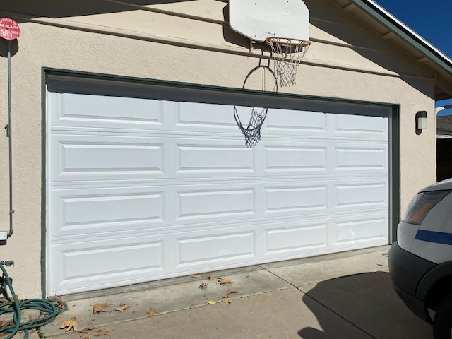 Close up view of garage door with basketball hoop above the door and light fixtures on one side.