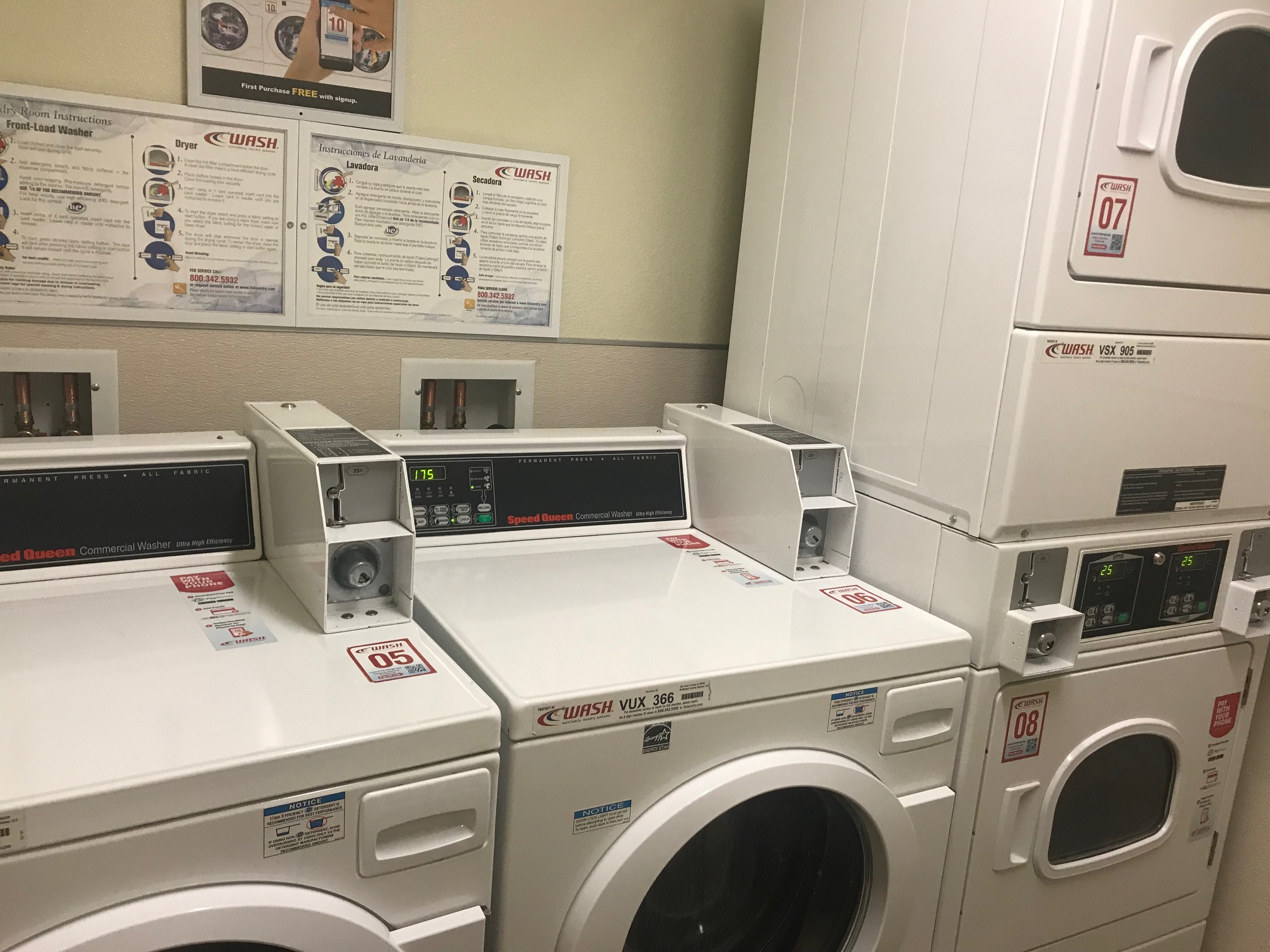 Laundry room with white appliances. Washer and dryer are coin operated. Washers are ground level and dryers are vertically double stacked. There are instructions posted on the wall on how to operate appliances.