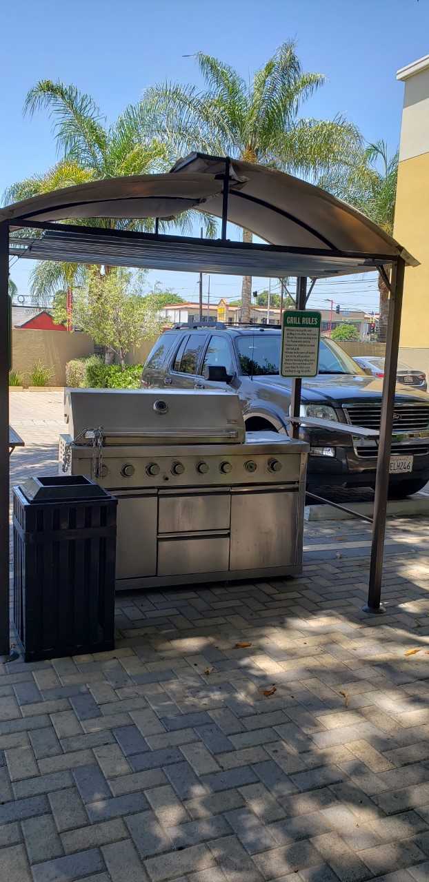 Rayen Apartments bbq area. Large stainless steel bbq grill located under shade covering. Trash reciprocal