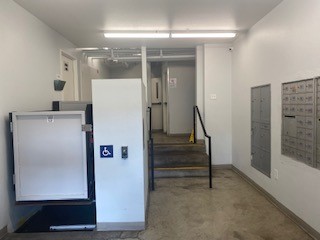 View of an ADA lift next to a small staircase with side bars. Mailboxes are also located in this section.