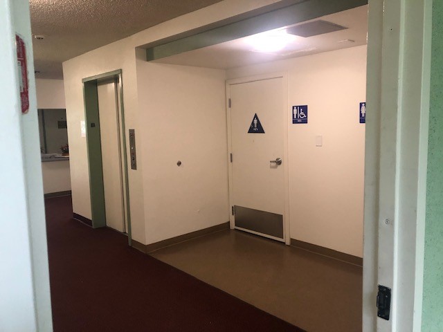 View of a Accessible restroom, an elevator on the left side, burgundy carpet, brown tile floor by the restroom.