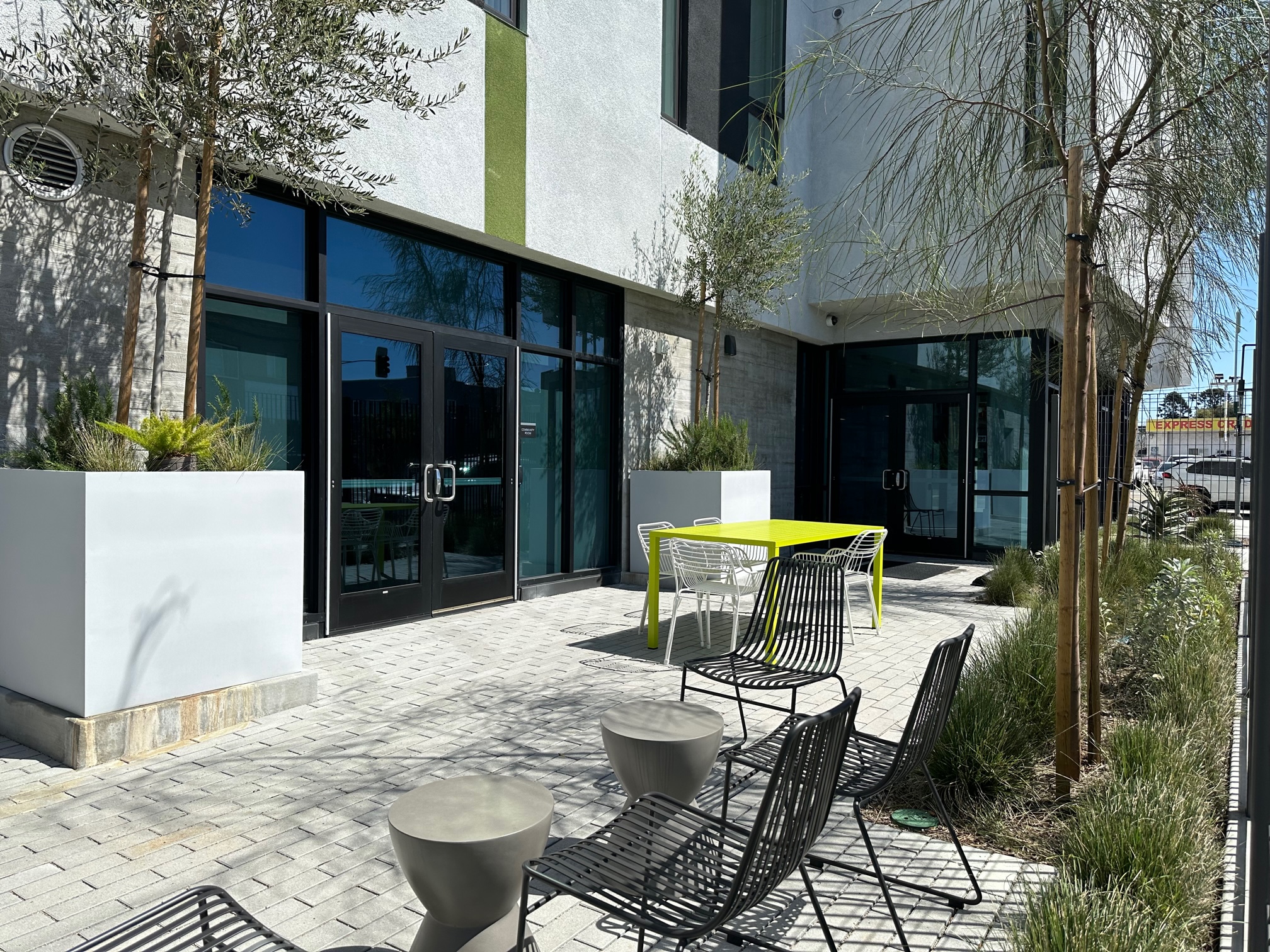 Property Pictures of outside the building. One yellow square table with 4 white metal chairs and additional sitting area on the side with 4 brown metal chairs and two small round tables.