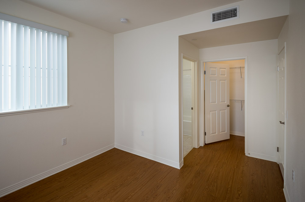 Inside view of a unit in Rio Vista Apartments. White walls with white blinds covering a window, slight view of the restroom and closet