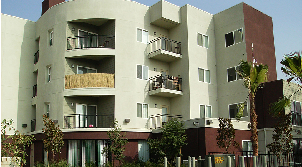 Maroon and pale green building, side view: balconies, young palms & shade trees