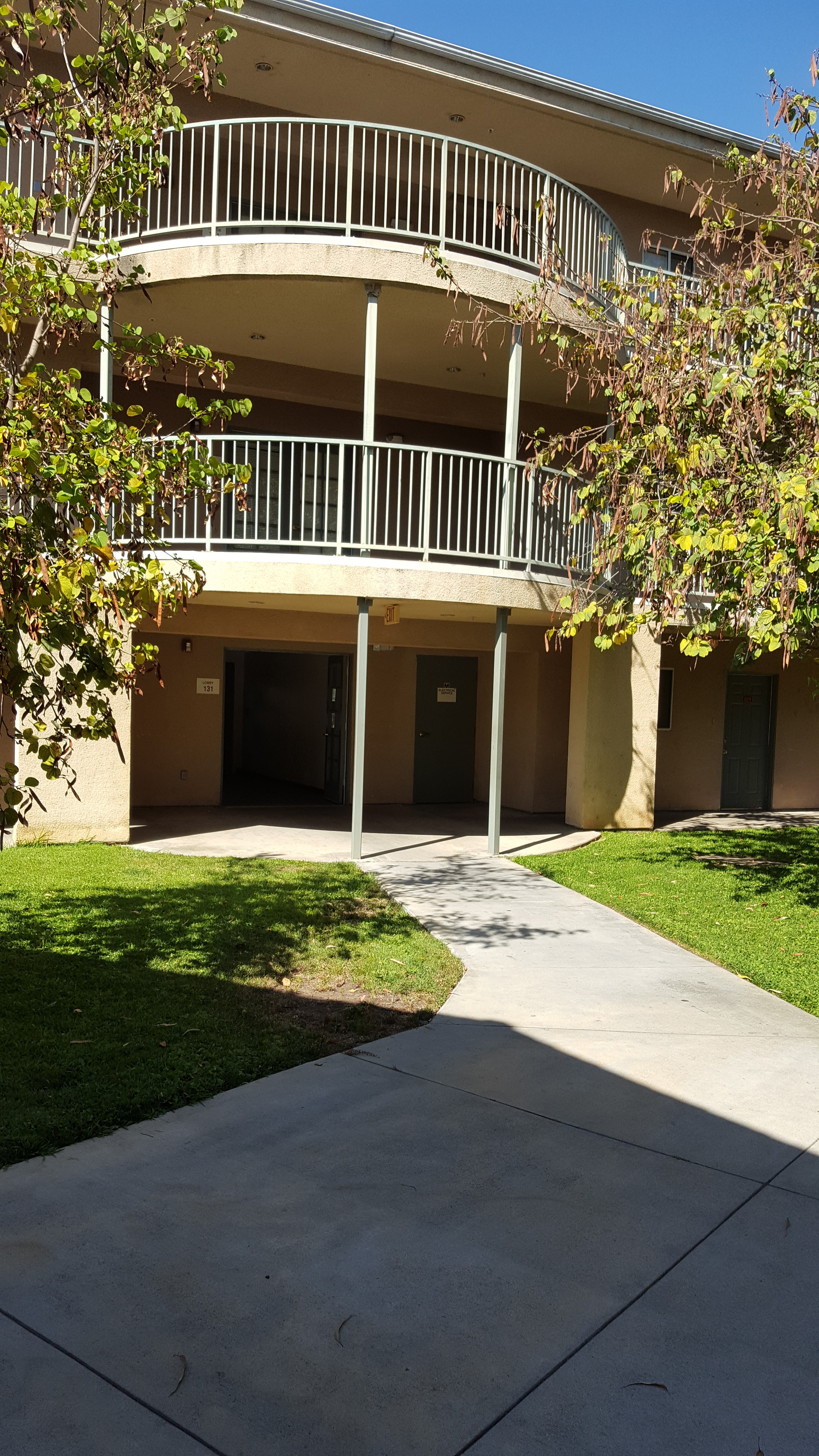 Front view of 3 floor building, grass and trees along sidewalk entry way