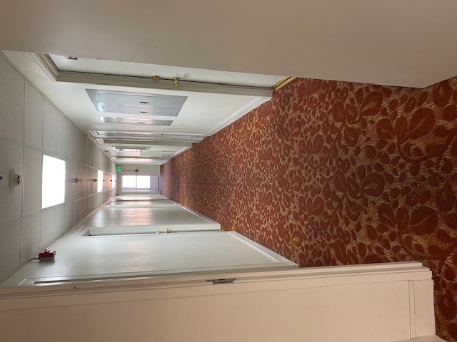 View of a hallway that leads to multiple units that is accessed through an open door. Floor is carpeted and ceilings have well lit lighting and sprinklers.