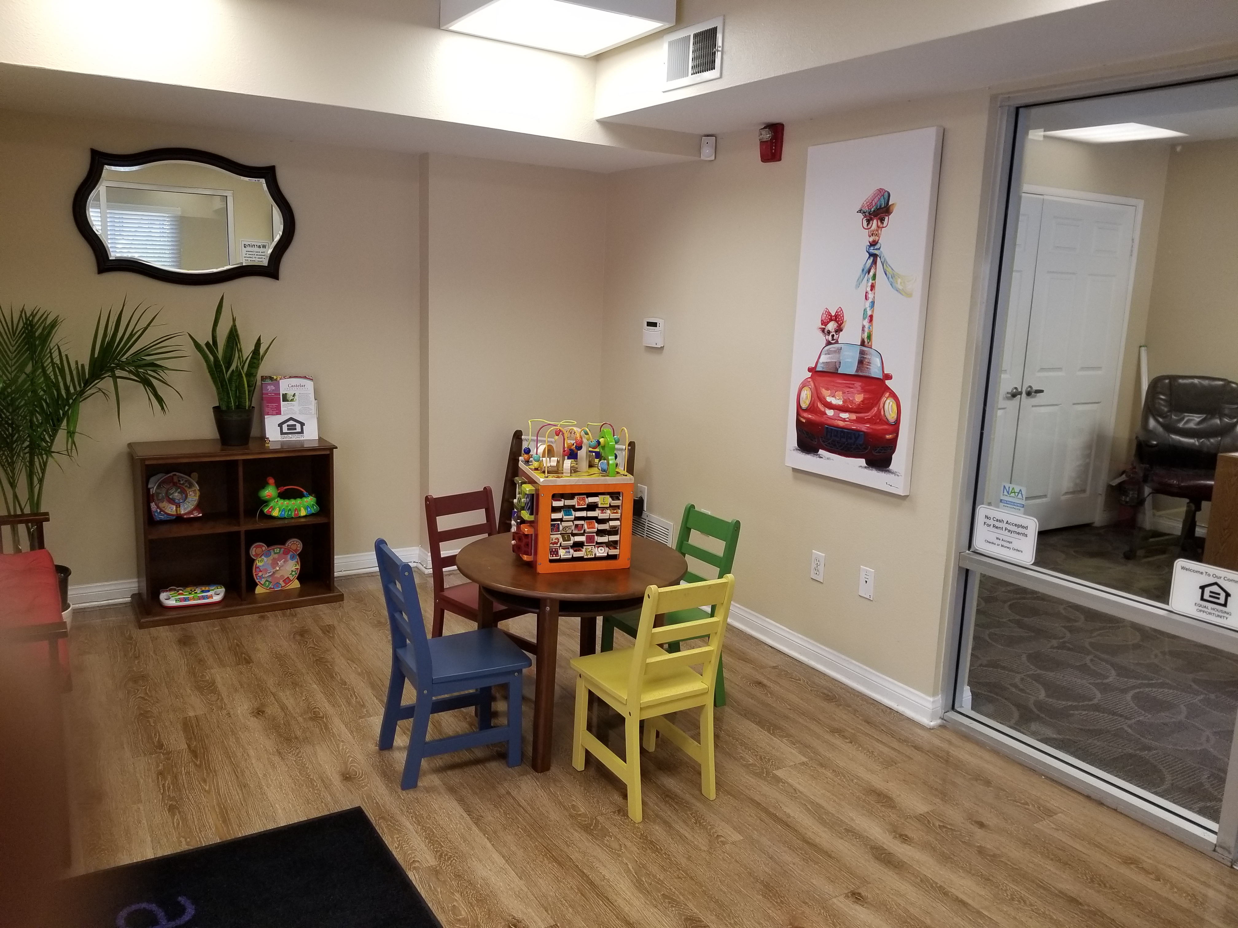 Interior view of a waiting area at the Castelar Apartments with children's table and a red, yellow, blue and green chair around. Childrens toys in cubbies and on top of table.
