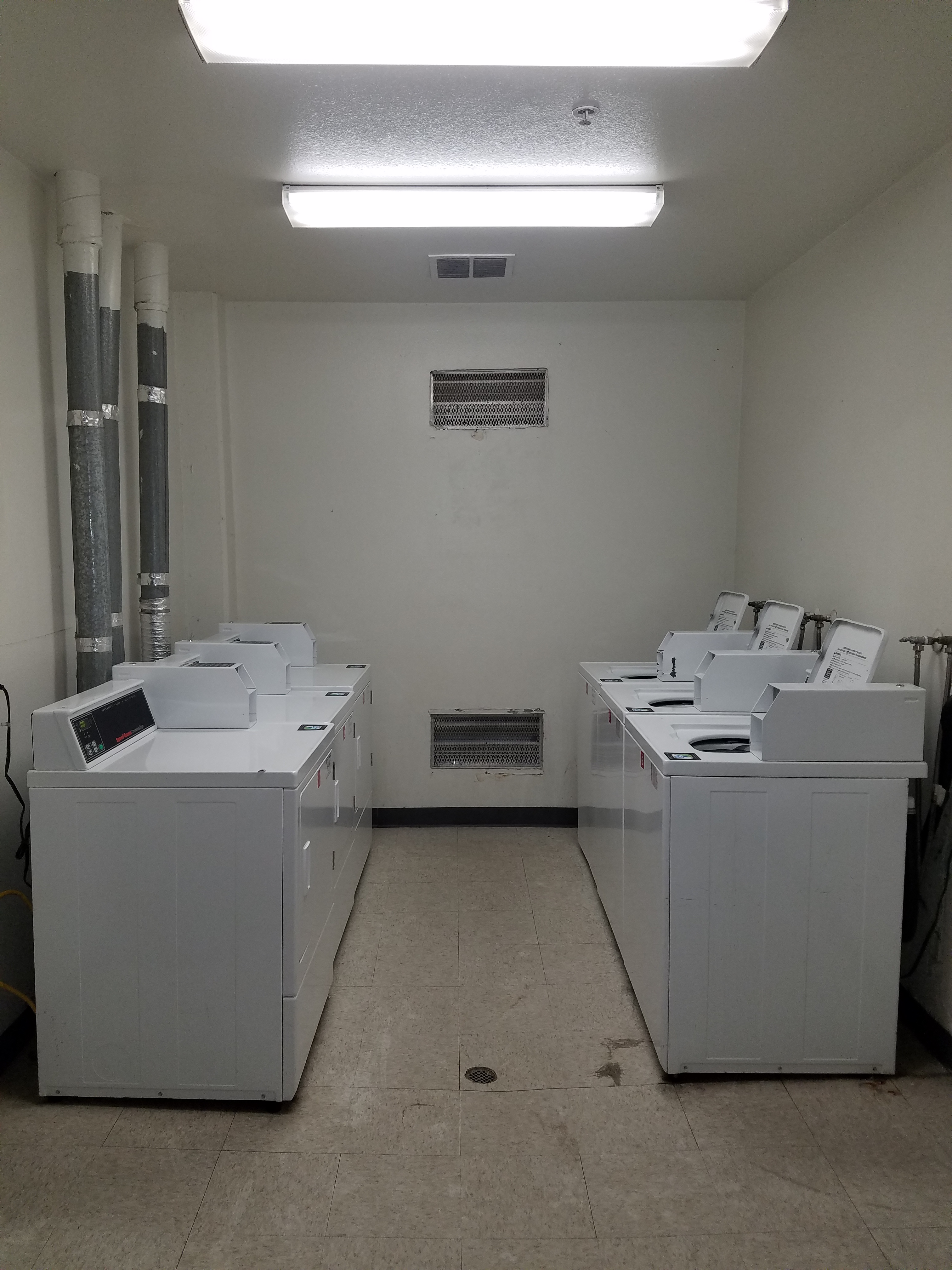 Parthenia Court laundry room. threewhite top load washers and across from them are three white front load dryers.