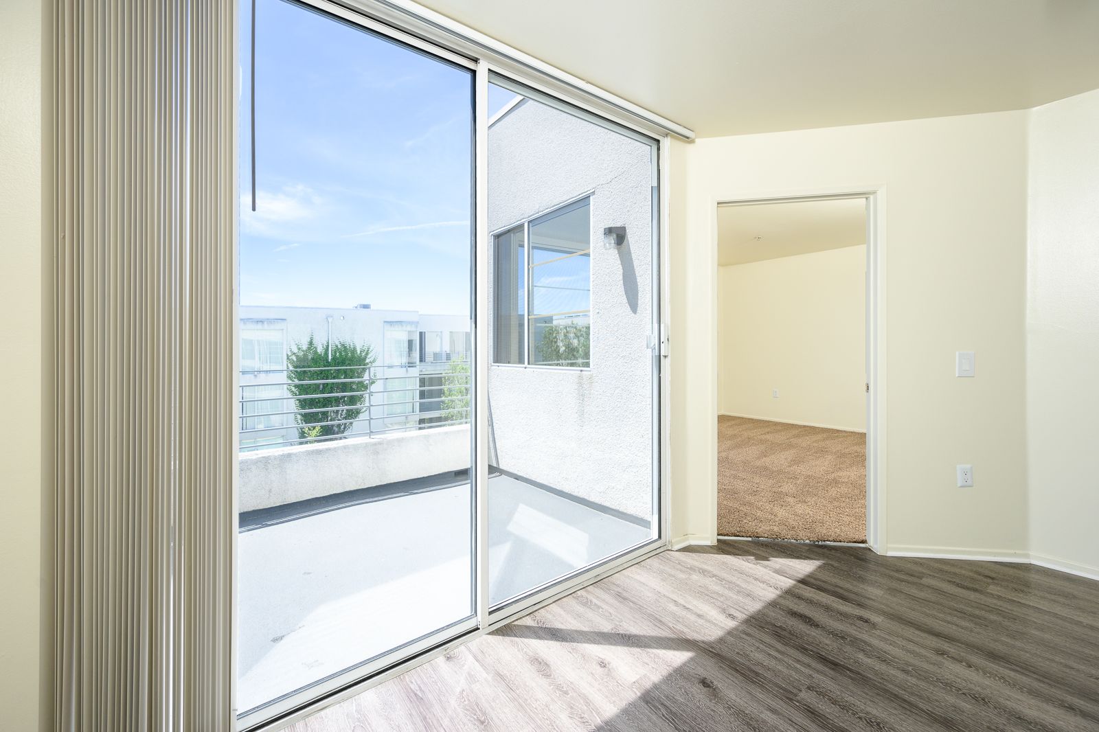 Balcony view from inside a vacant unit. Wood flooring leads to a large, glass sliding door that opens to an outdoor balcony.