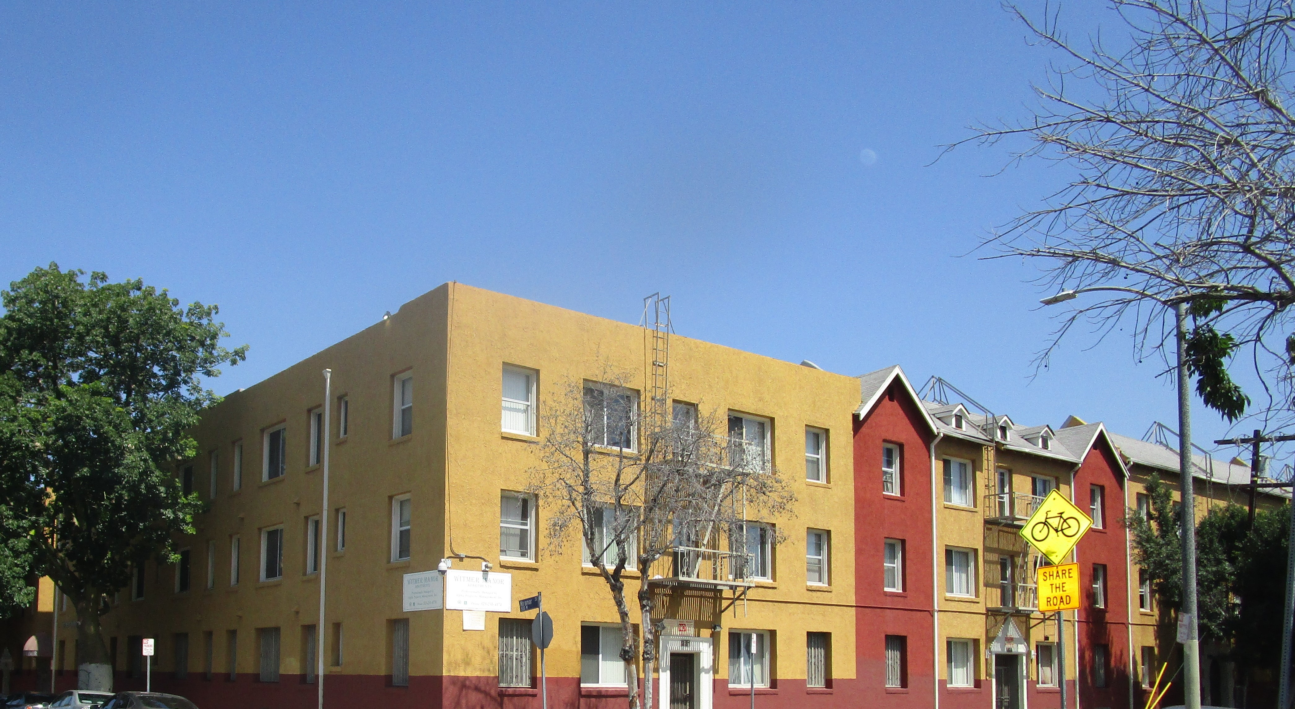 Front corner view of a four story yellow and red building. There are two fire escapes in the front of the building.
