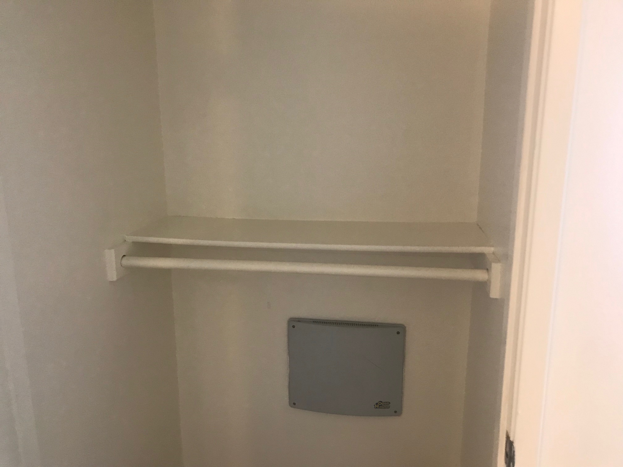 View of a small closet that containg a hanger bar and a shelf.