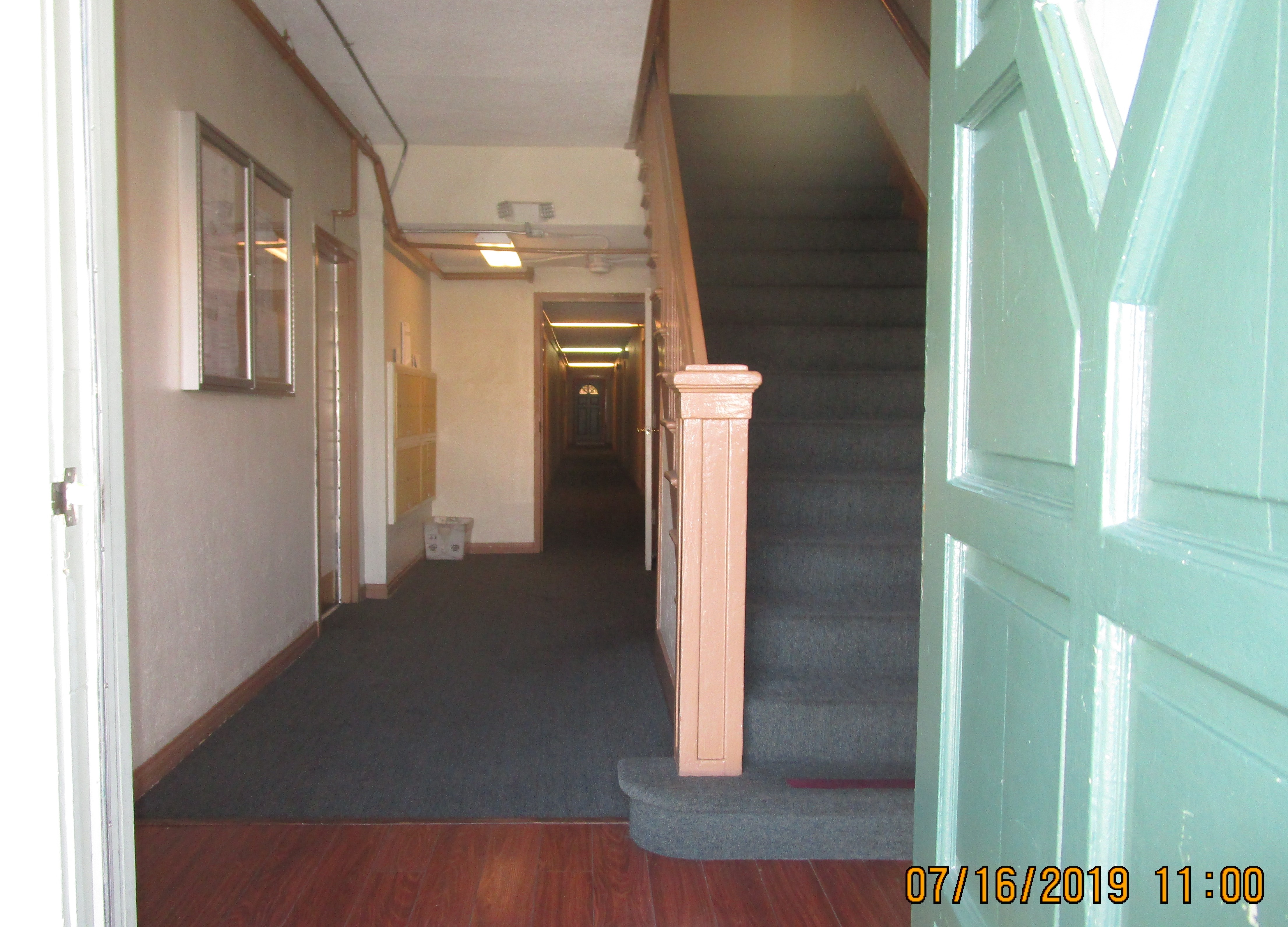 Stairs on right side and a long hallway along the length of the building on the left side. Mailbox area and bulletin board on the left side.