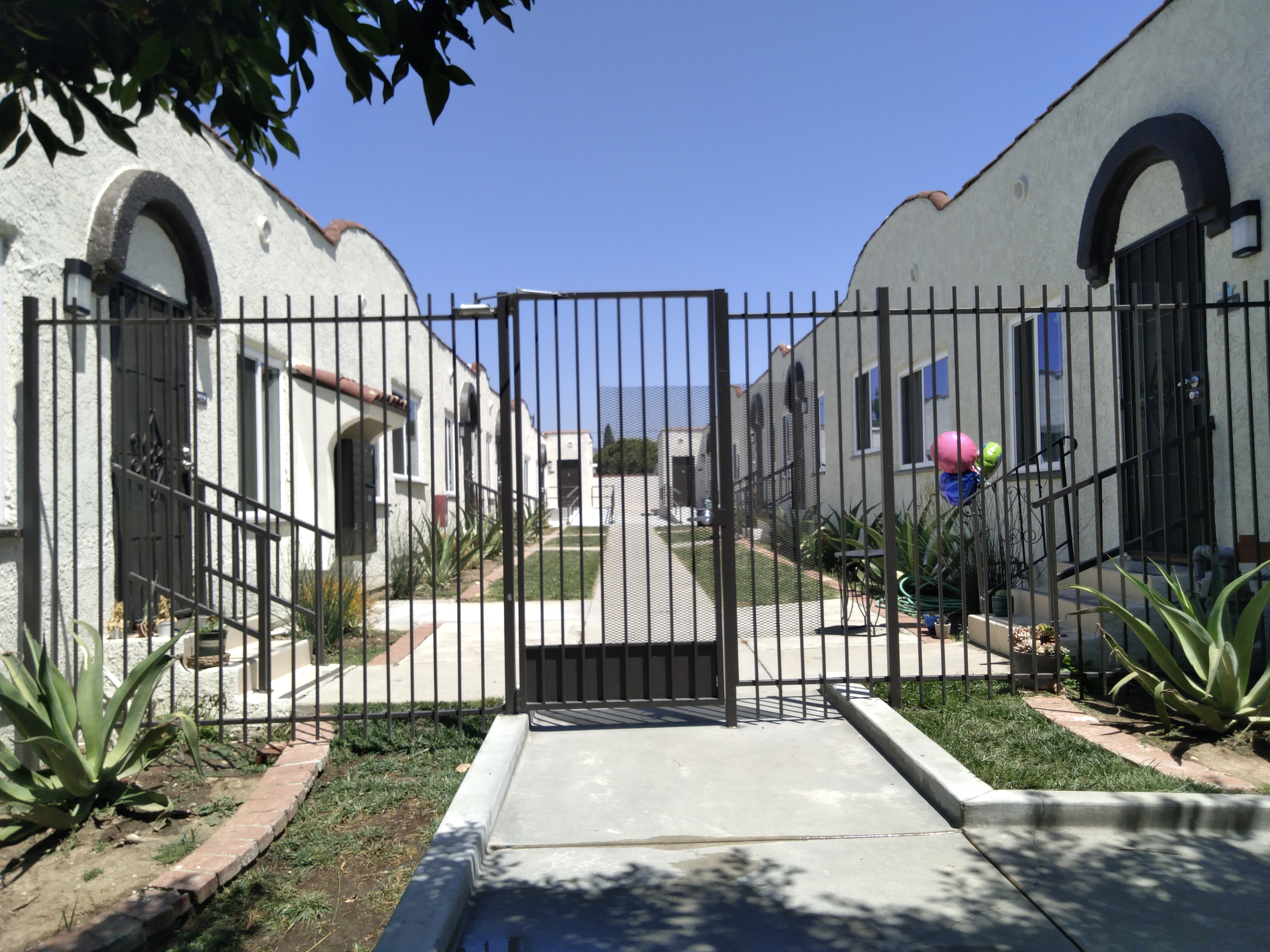 Black steel front gate, courtyard style, each apartment with a three step and handrail entrance, Aloe vera plant on each side of the main entrance and all along next to each apartment. Colorful ballons in front of one apartment
