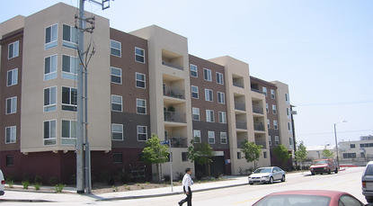 Outside view of the apartment building. The building is brown and light brown. The building is surrounded by trees.