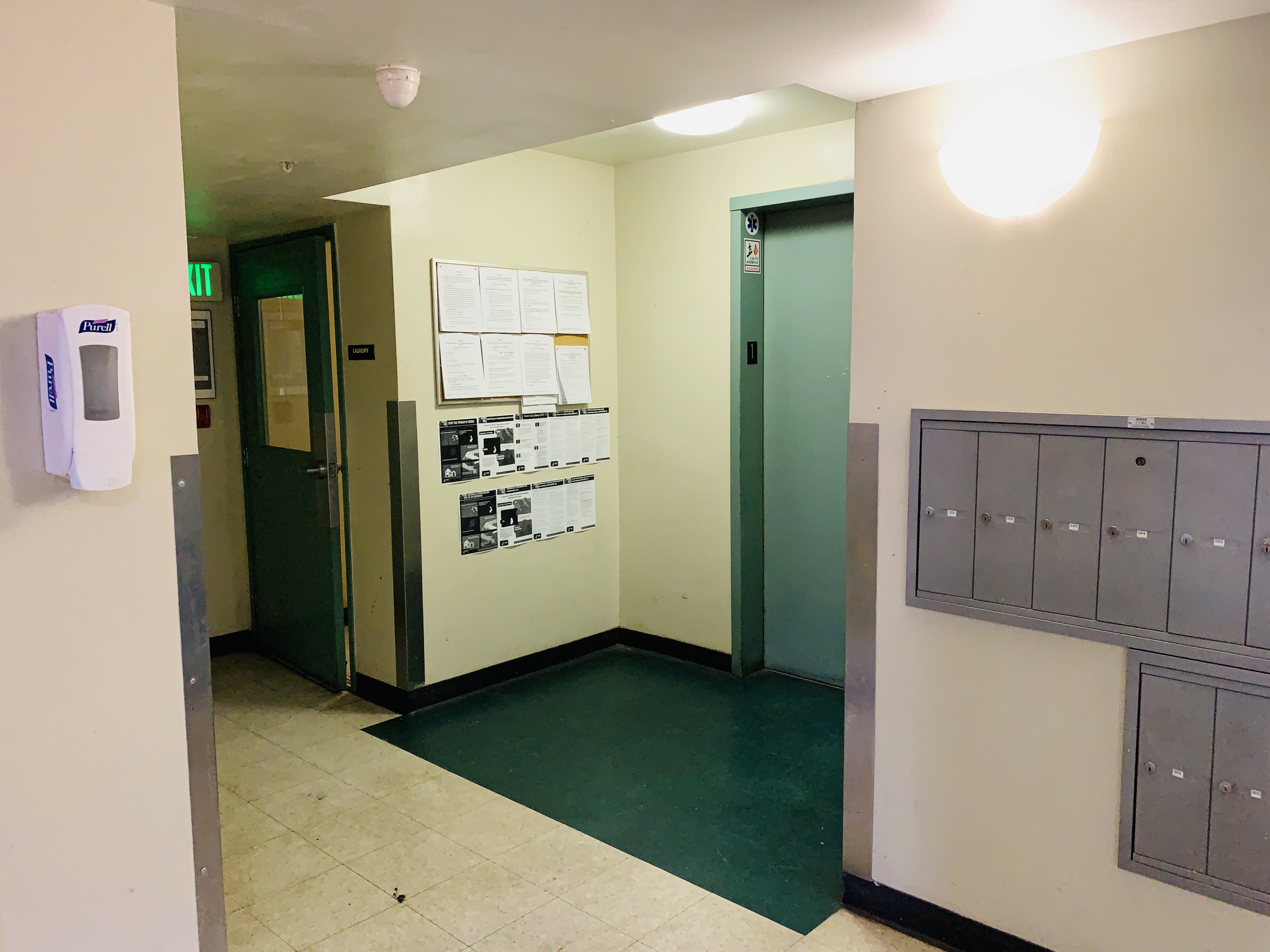 View of lobby, elevator, mailboxes on the right side, and a board with multiple flyers hanging on the left side wall.