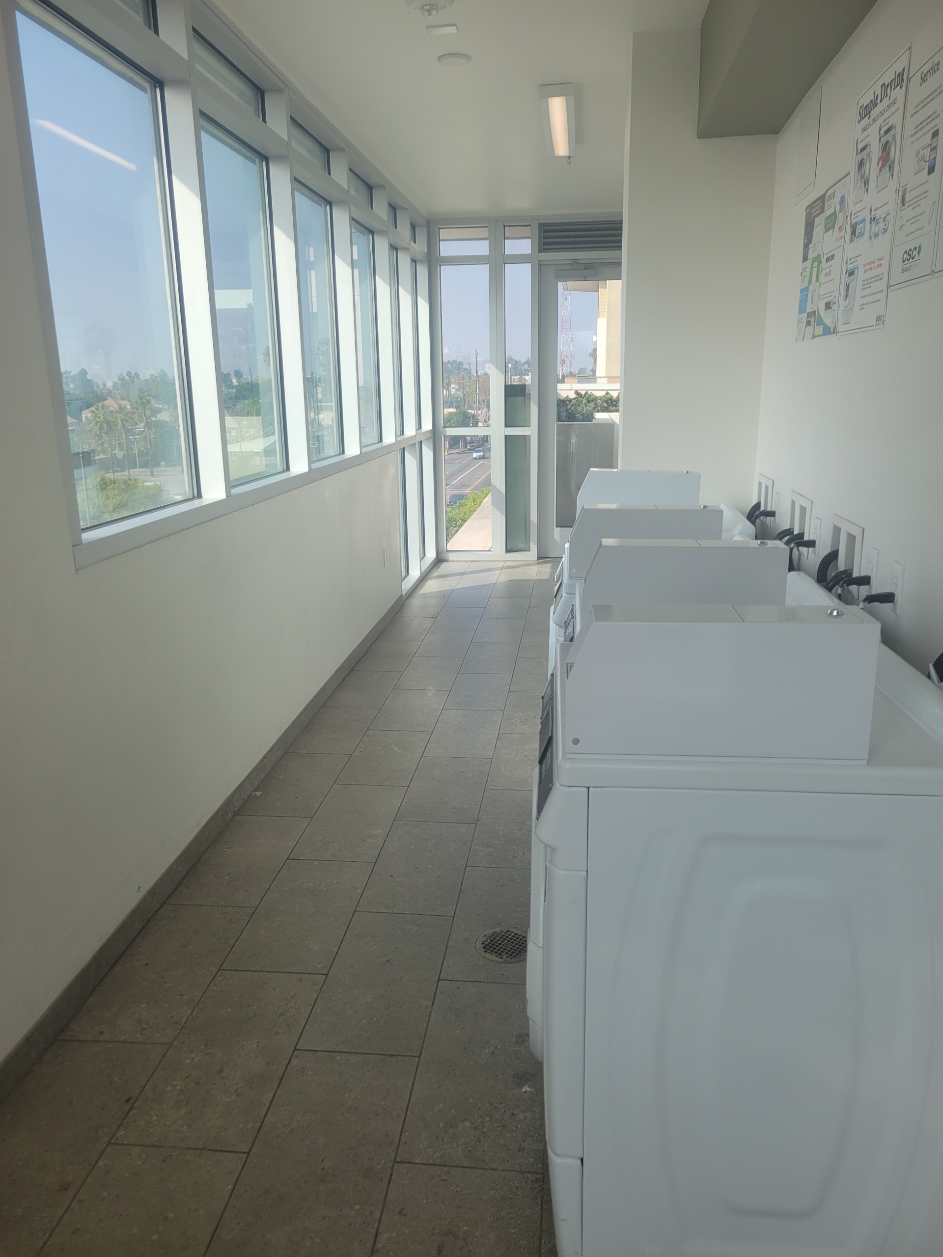 CLII laundry room Machines line the right wall. Windows line the left. At the end there is a big window.