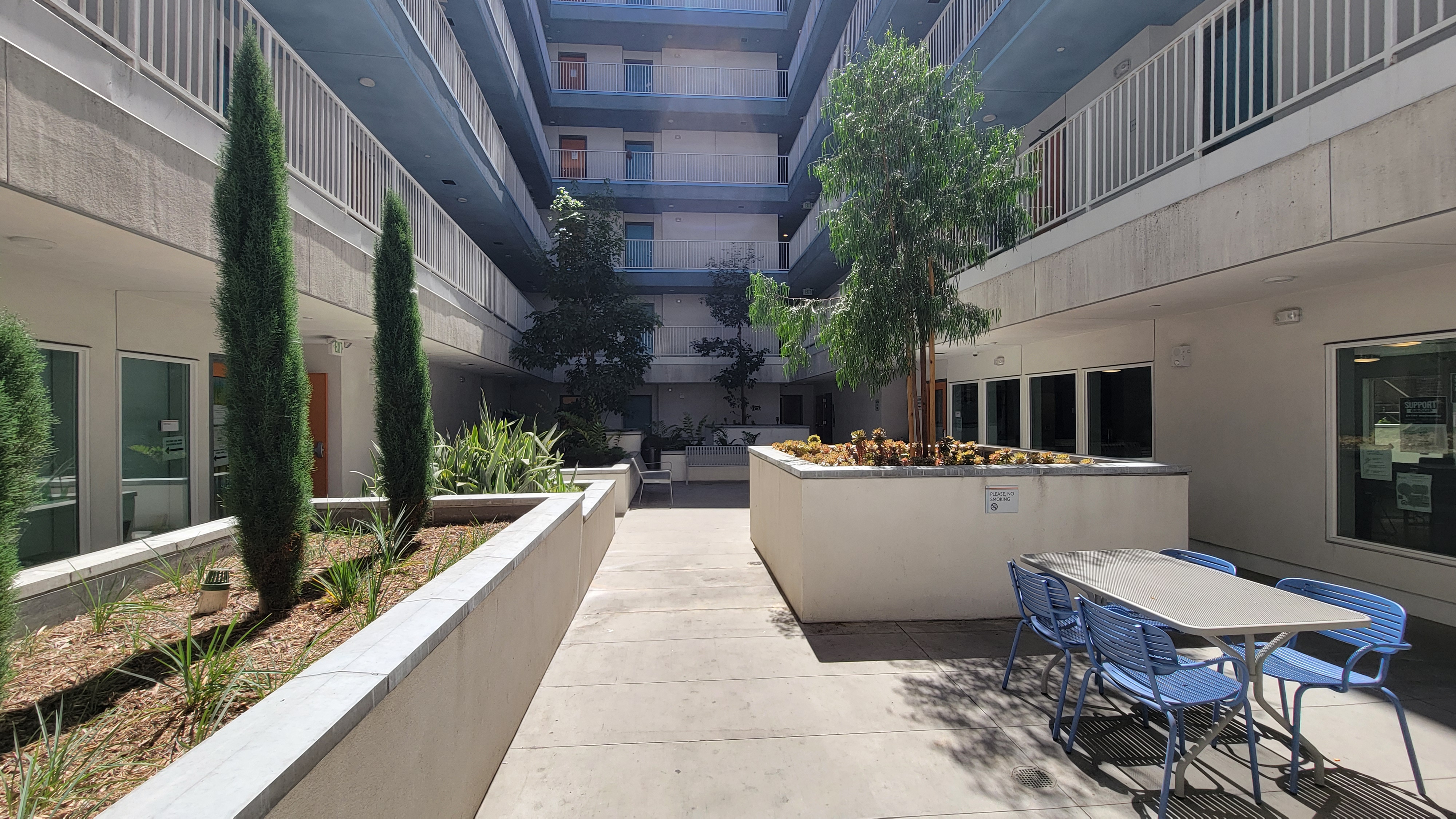 Courtyard with view of upper levels of building. Planters on either side with a table and benches for sitting on the far end.