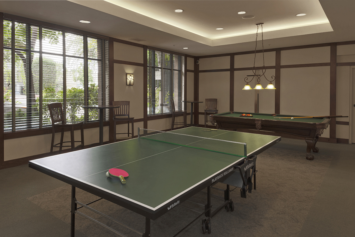 Common room that consists of a pool table and a ping pong table. There are a couple of high chairs and high tables. Room has large windows with horizontal blinds.