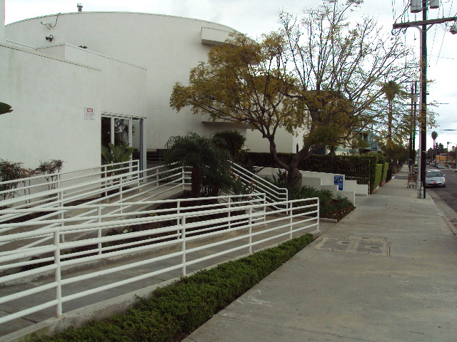 White handrails around a concrete ramp, many trees and bushes.