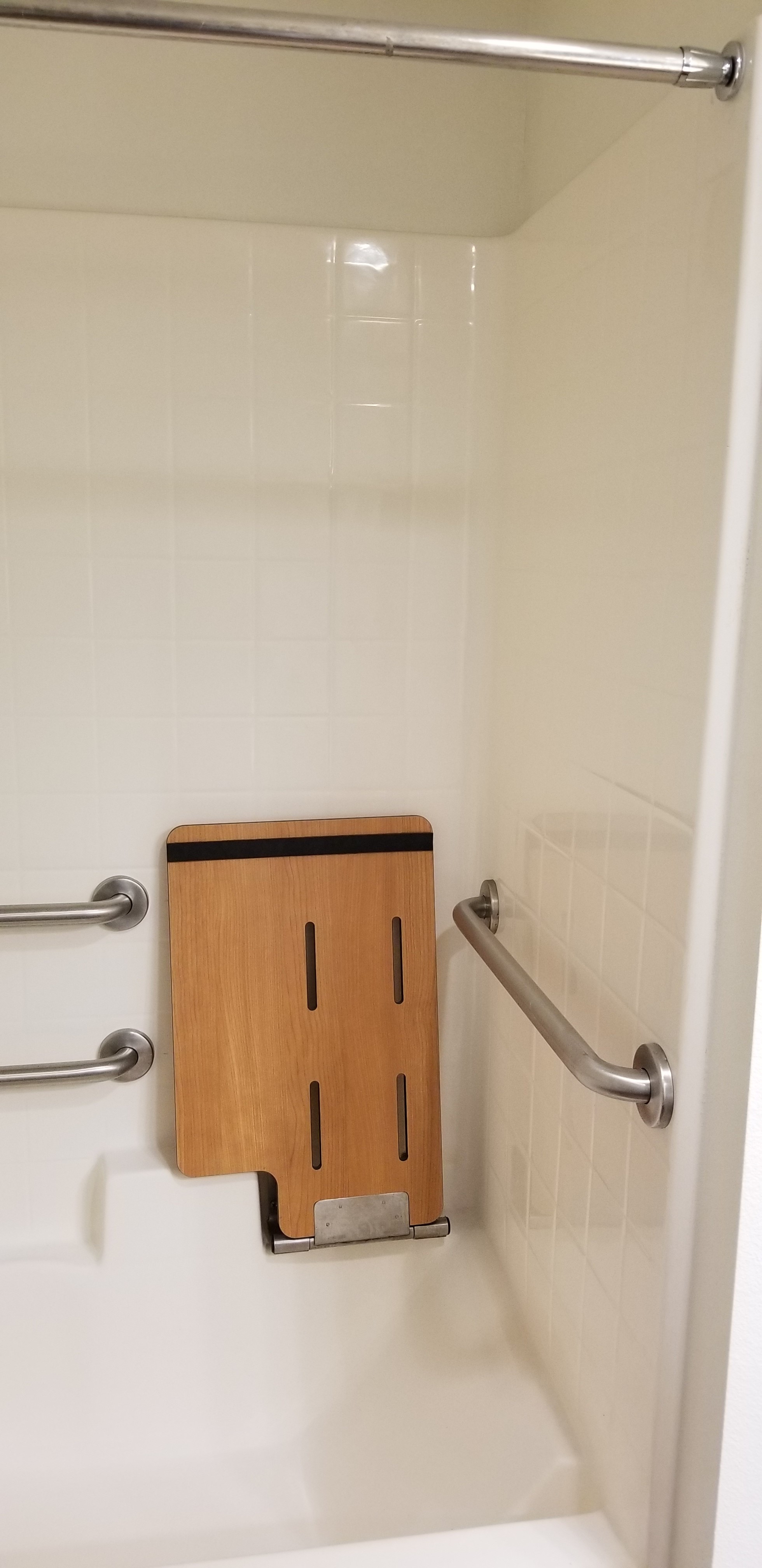 View of Morgan Place unit shower. Shower as foldable shower bench. Grab bars located in the shower to the back and side of shower bench.