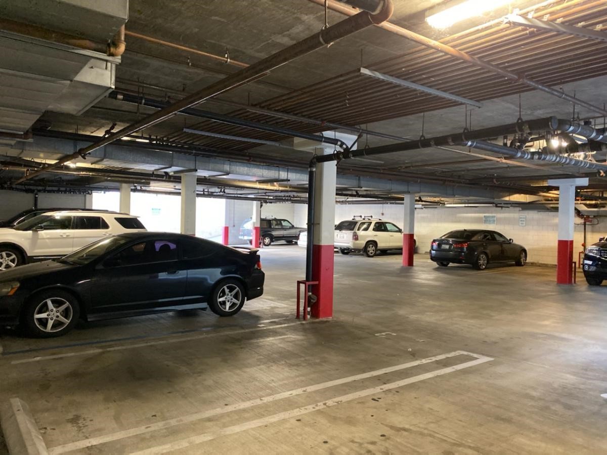 Inside view of a multi car garage parking lot. Ceiling has pipes and lighting across it.