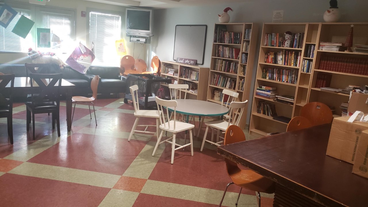 Photo of Community Room, tables, chairs, TV, whiteboard, books on book shelves