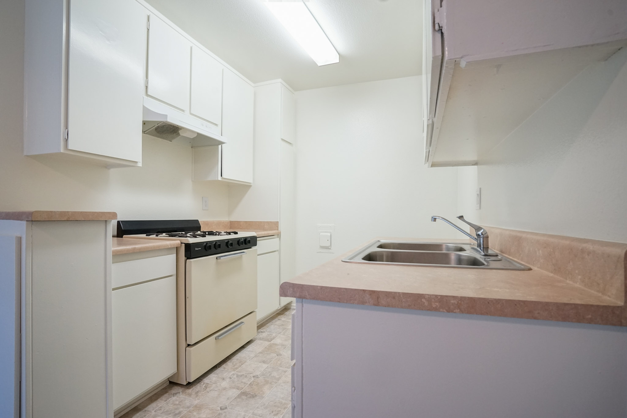 Different angle of the kitchen area. There is a stove and a sink across from it. Both sides have small counter space, and there are upper and lower cabinets.