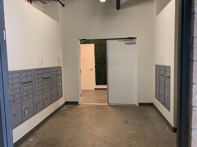 Interior view of mail room area. Room has double doors entry and gray mailboxes on two walls across each other.