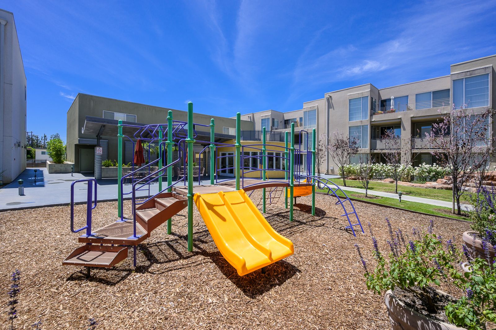 Large, outdoor playground set on top of woodchips.  Small grassy area with trees on the side.