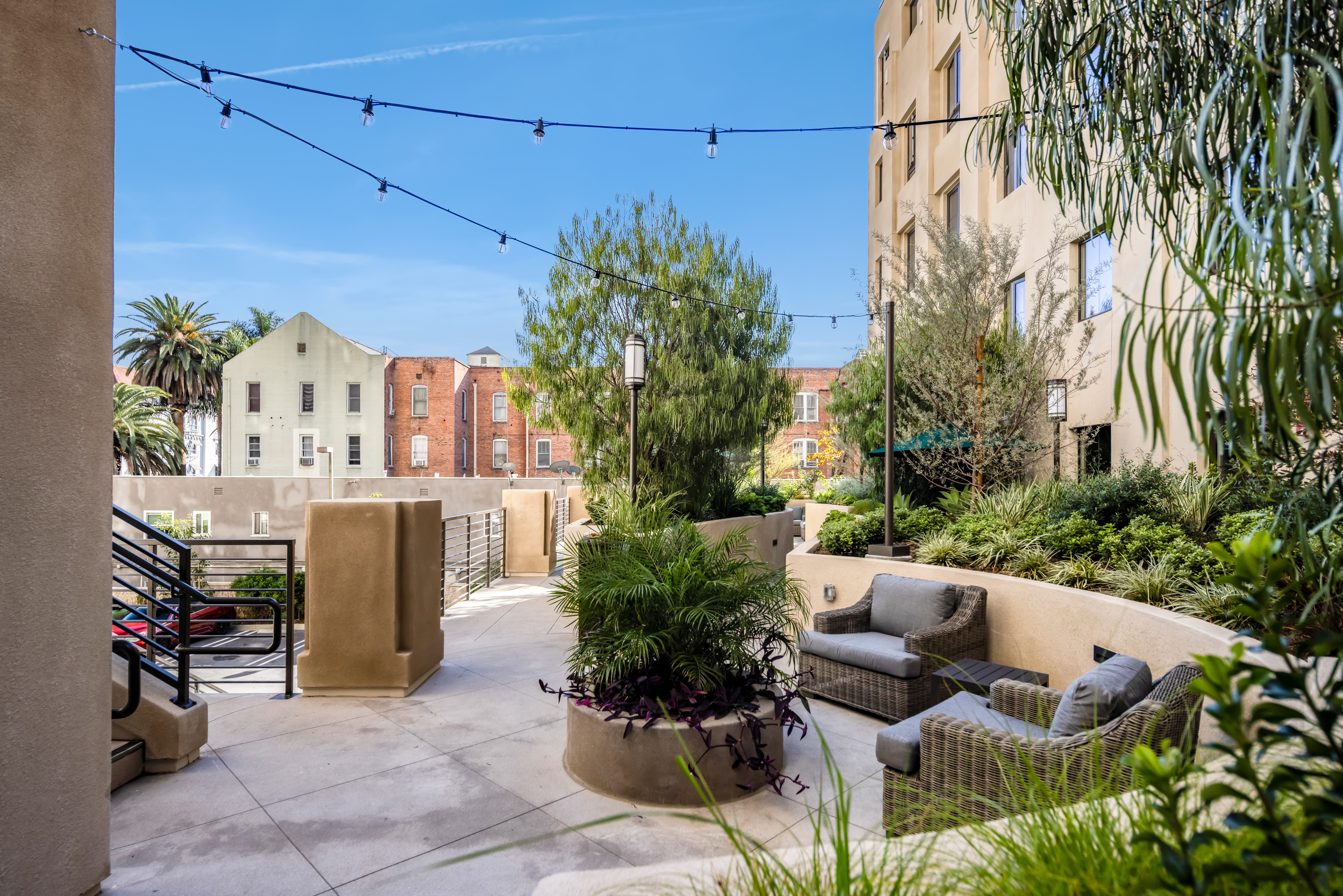 Cozy patio with wicker furniture and foliage, surrounded by strings of fairy lights on a sunny day.