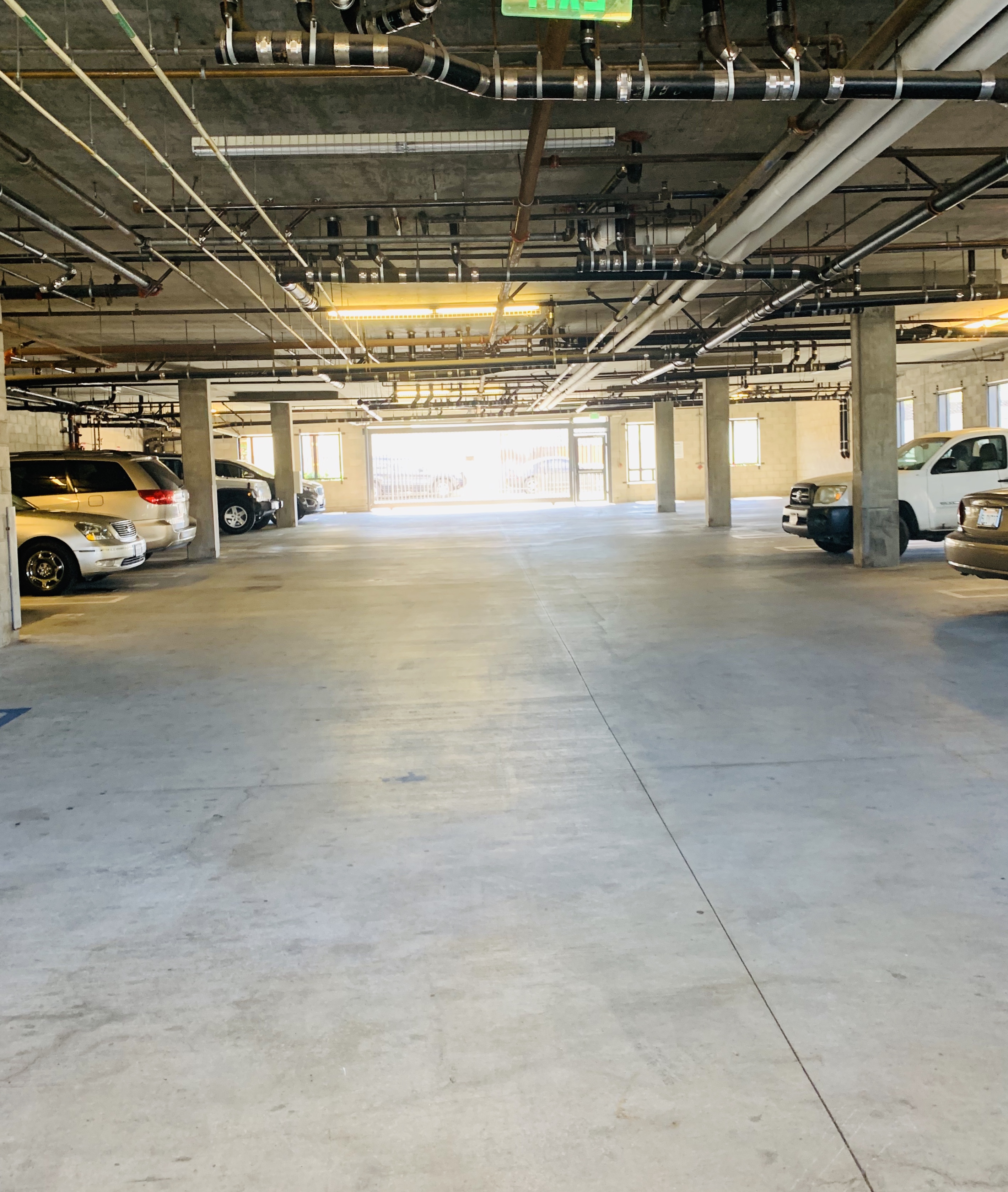 Inside view of a gated parking garage. Gargae has multiple parking spaces and pipes and lighting on the ceiling.